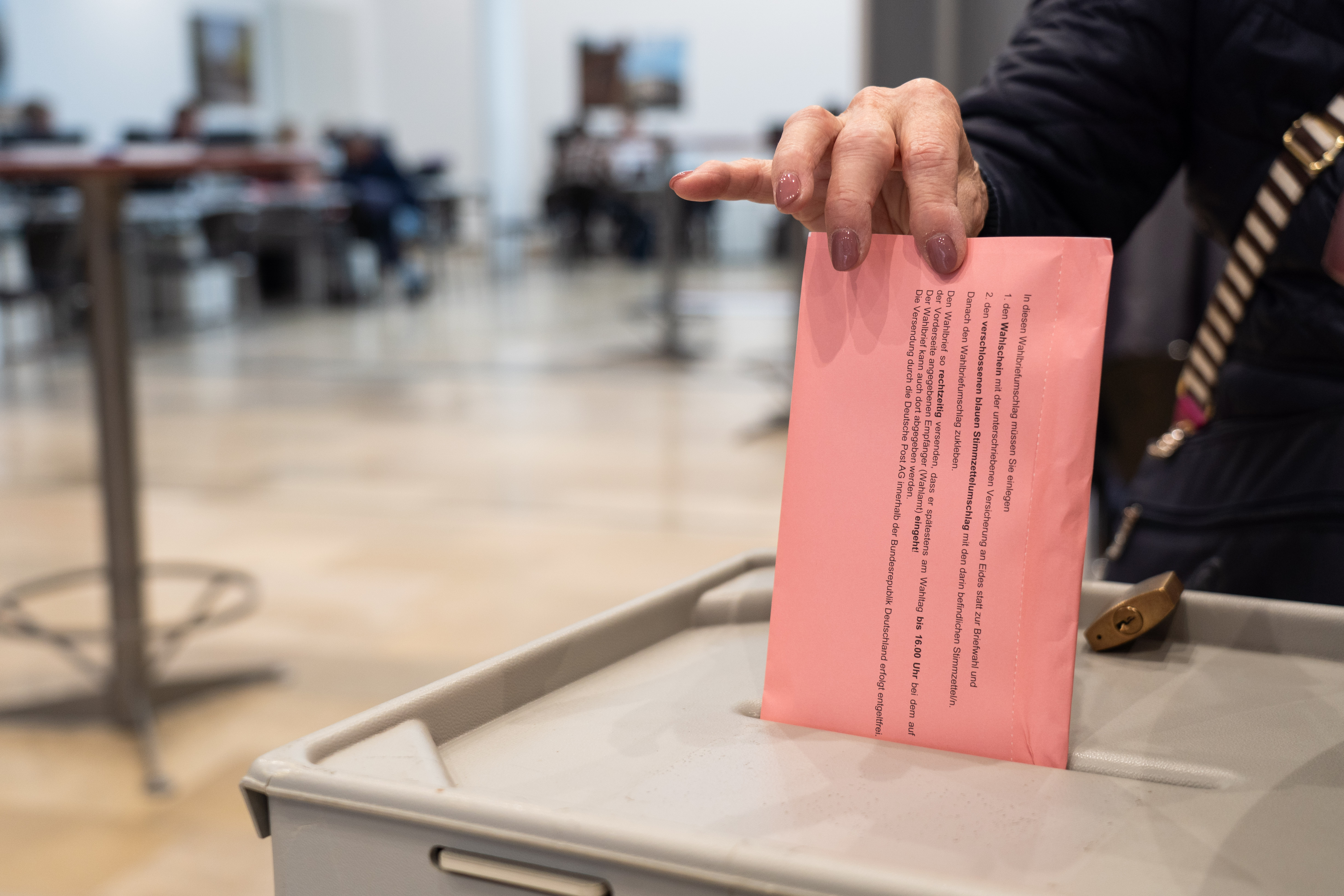 Eine Hand wirft einen roten Wahlbrief in die Wahlurne