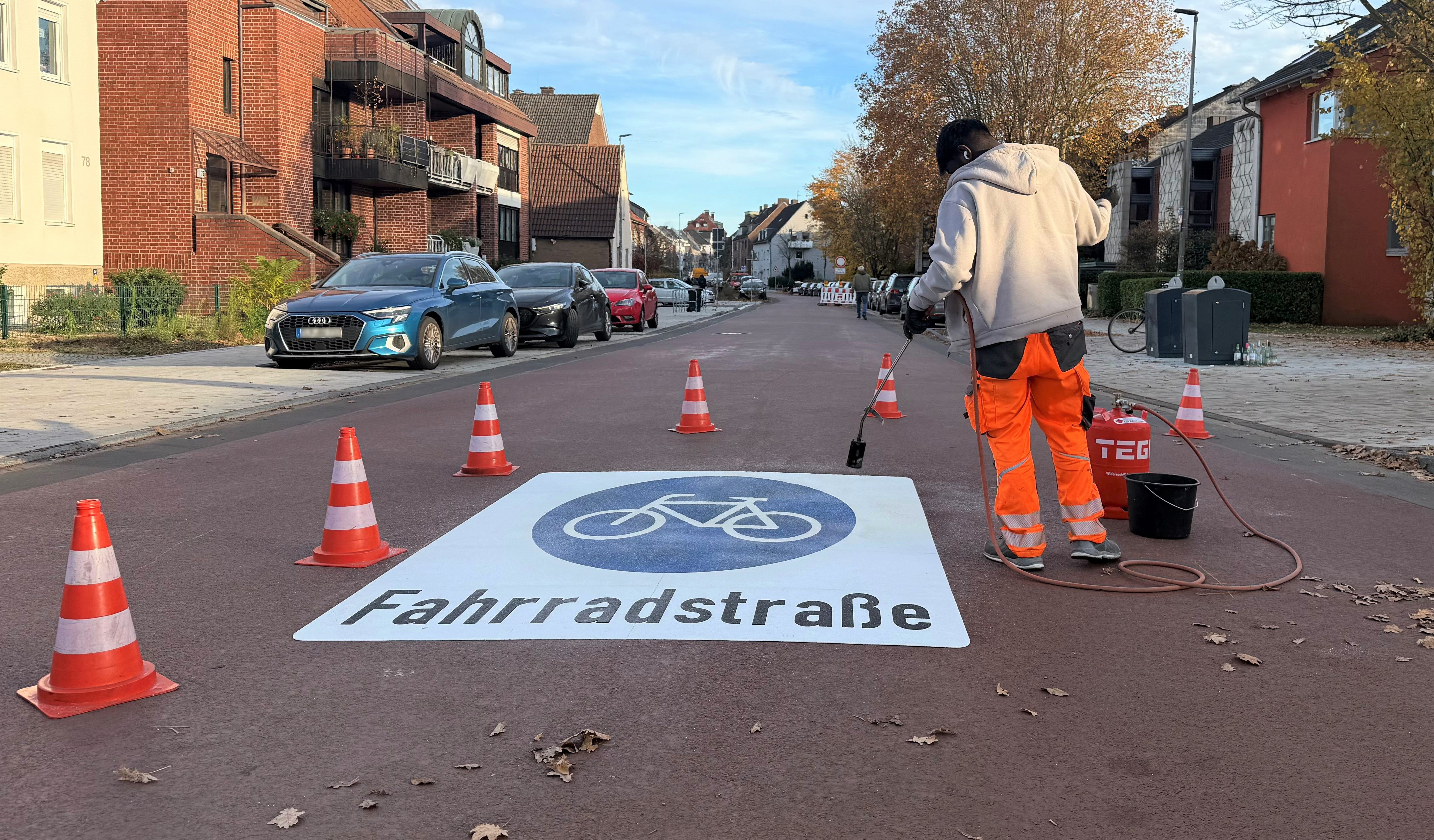 Ein Arbeiter bringt auf der roten Straße das Pictogramm "Fahrradstraße" an
