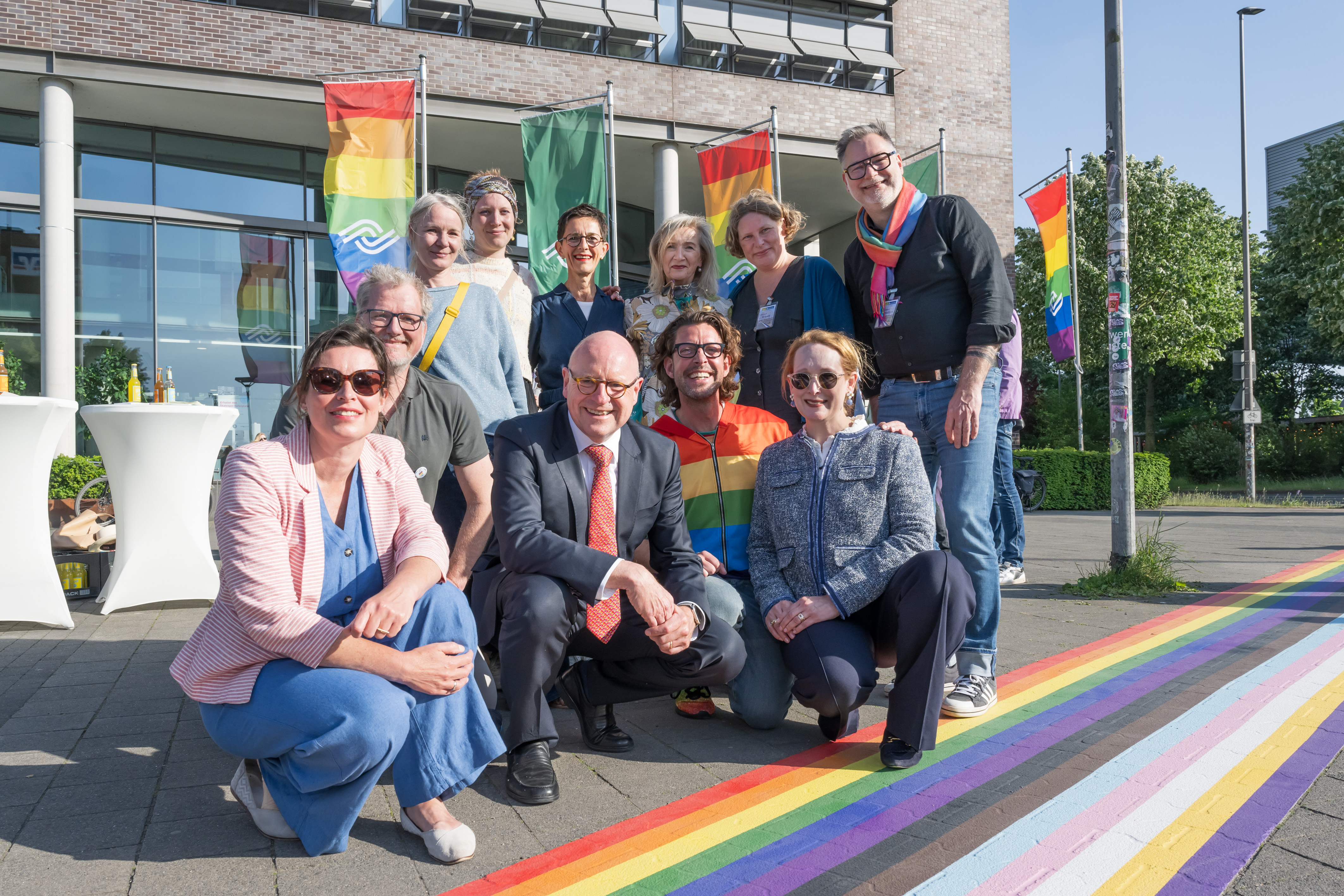 Zehn Personen hocken oder stehen neben dem Regenbogenstreifen