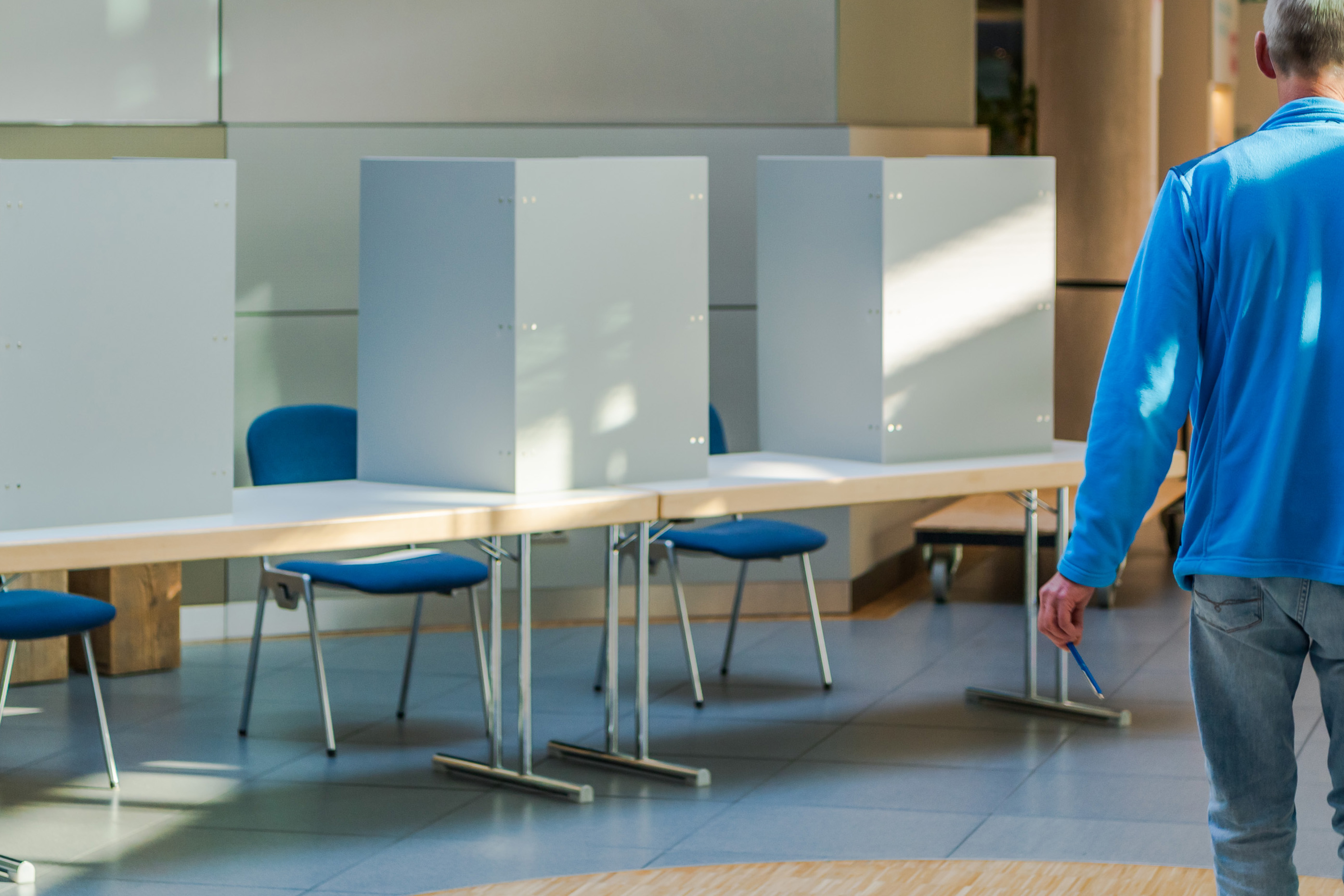Ein Mann geht auf einen Tisch zu, auf dem dem drei Wahlkabinen aufgebaut sind.