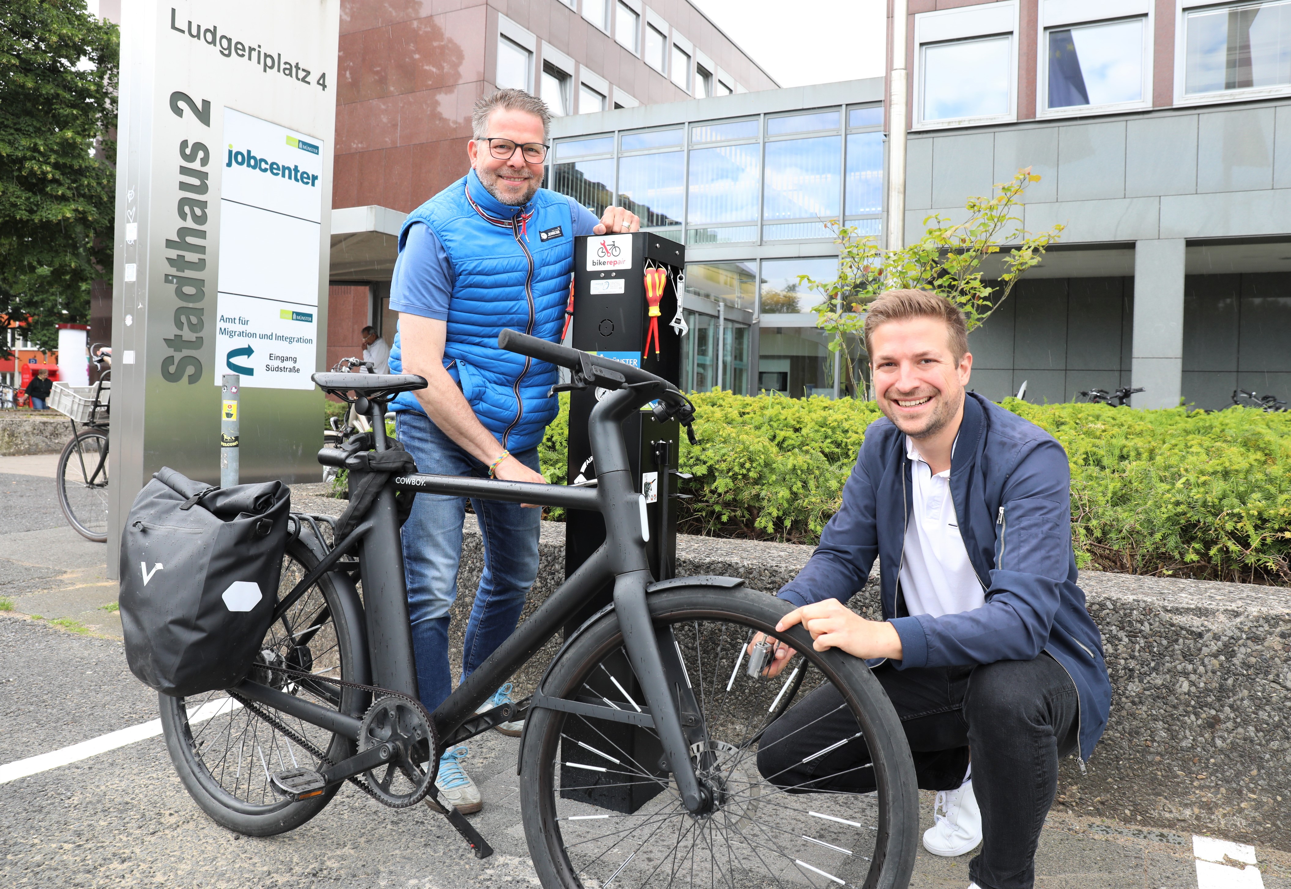 Eine Person steht an einem Fahrrad und hält es, eine zweite Person hockt davor.