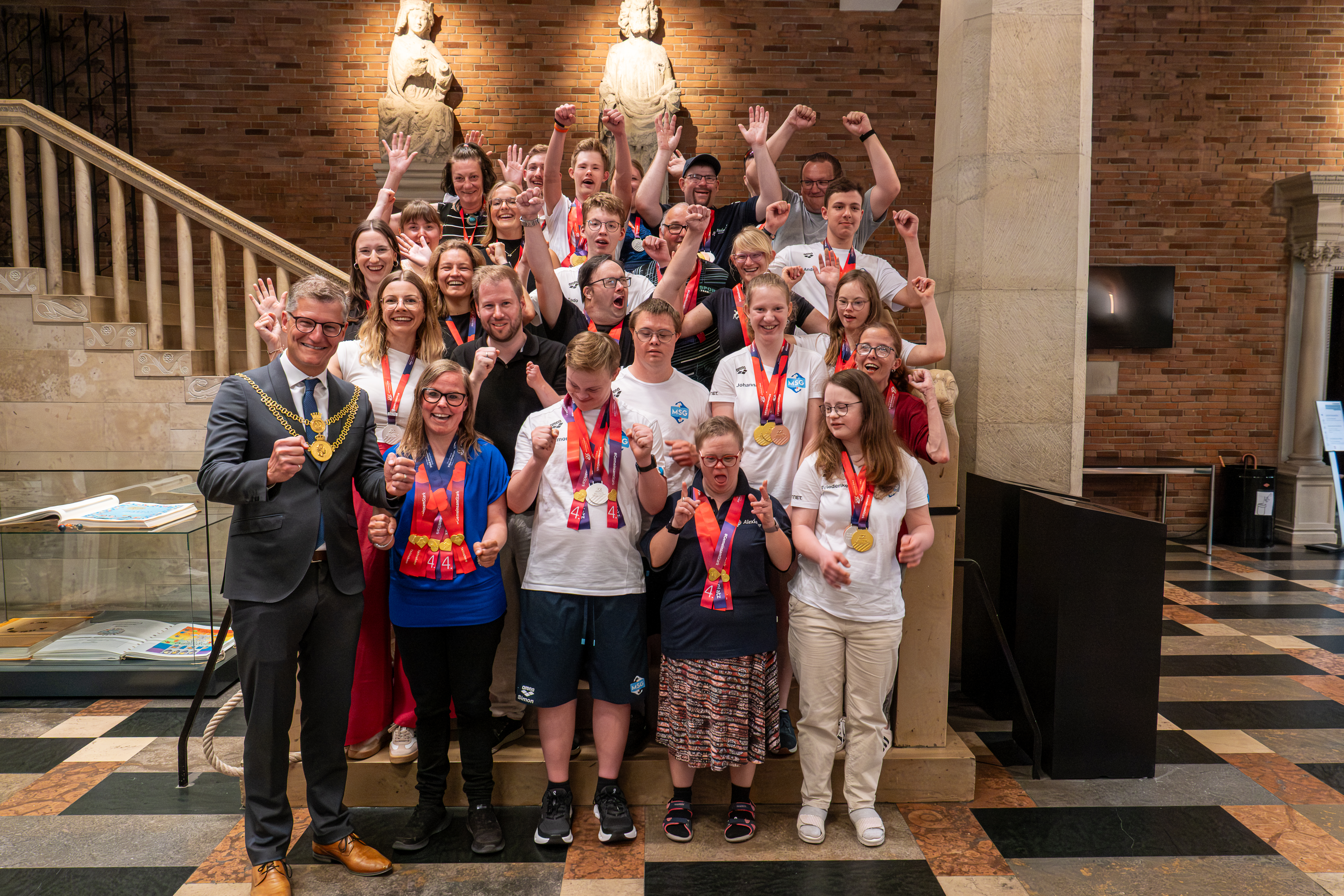 Special-Olympics-Teilnehmenden stehen zusammen mit ihren Begleitenden auf einer Treppe im Rathaus zusammen mit Oberbürgermeister Tilman Fuchs