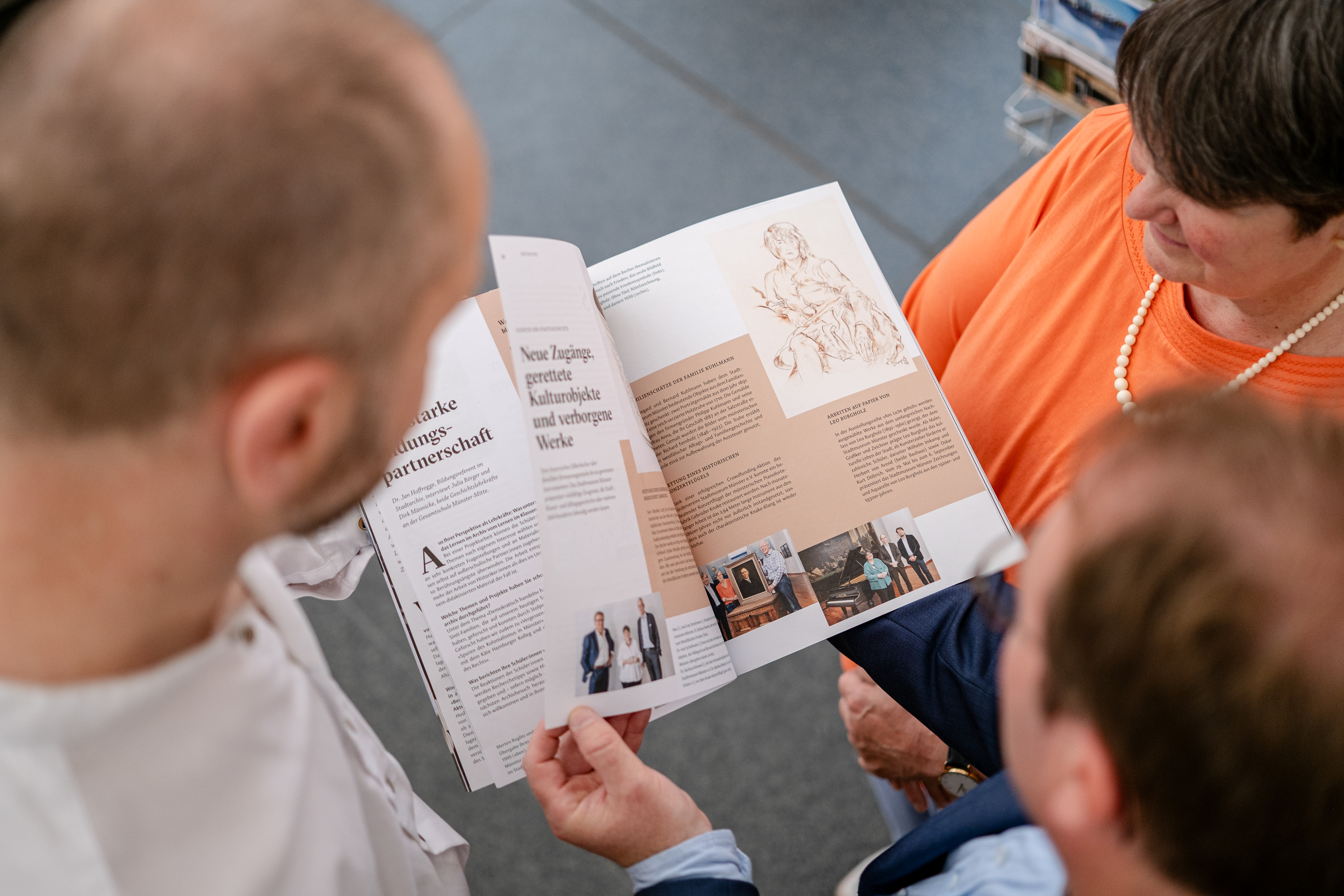 Drei Menschen von oben zu sehen, in ihrer Mitte halten sie das neue Kulturmagazin und blättern darin. 