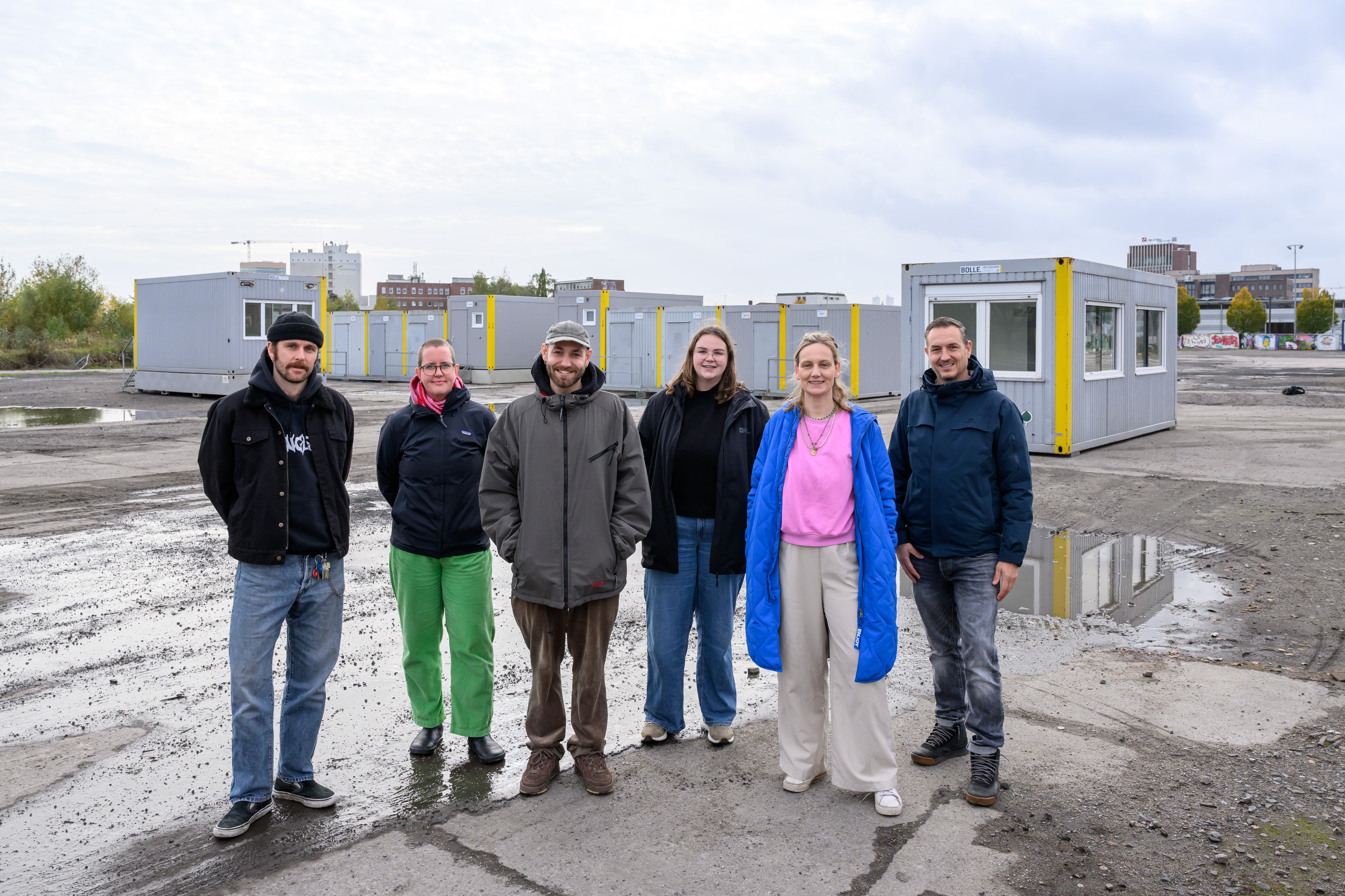 Gruppenfoto von sechs Personen; im Hintergrund stehen Container auf einer freien Fläche