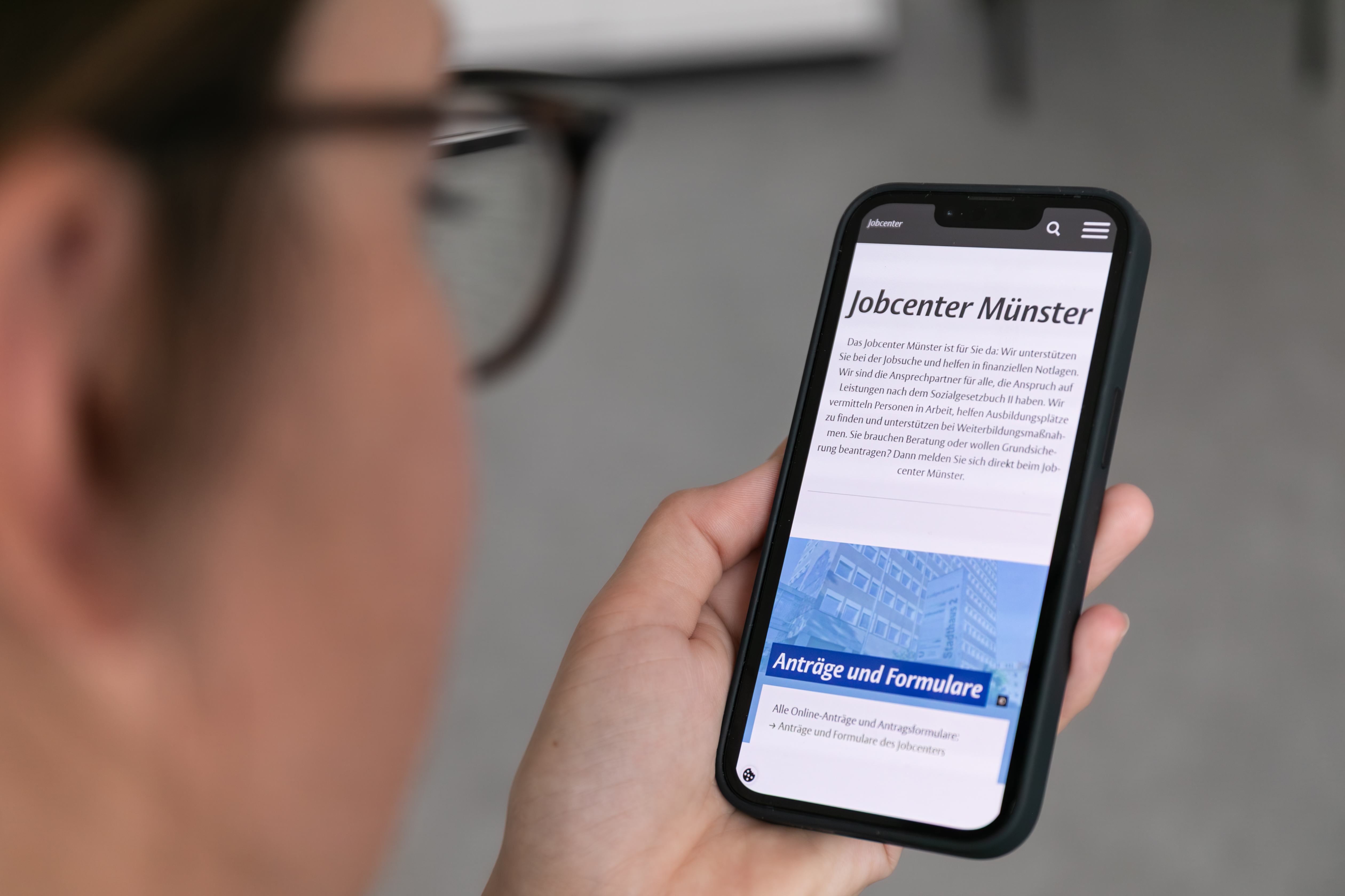 Eine Frau schaut auf ein Smartphone auf dem die neue Jobcenter-Webseite zu sehen ist. 