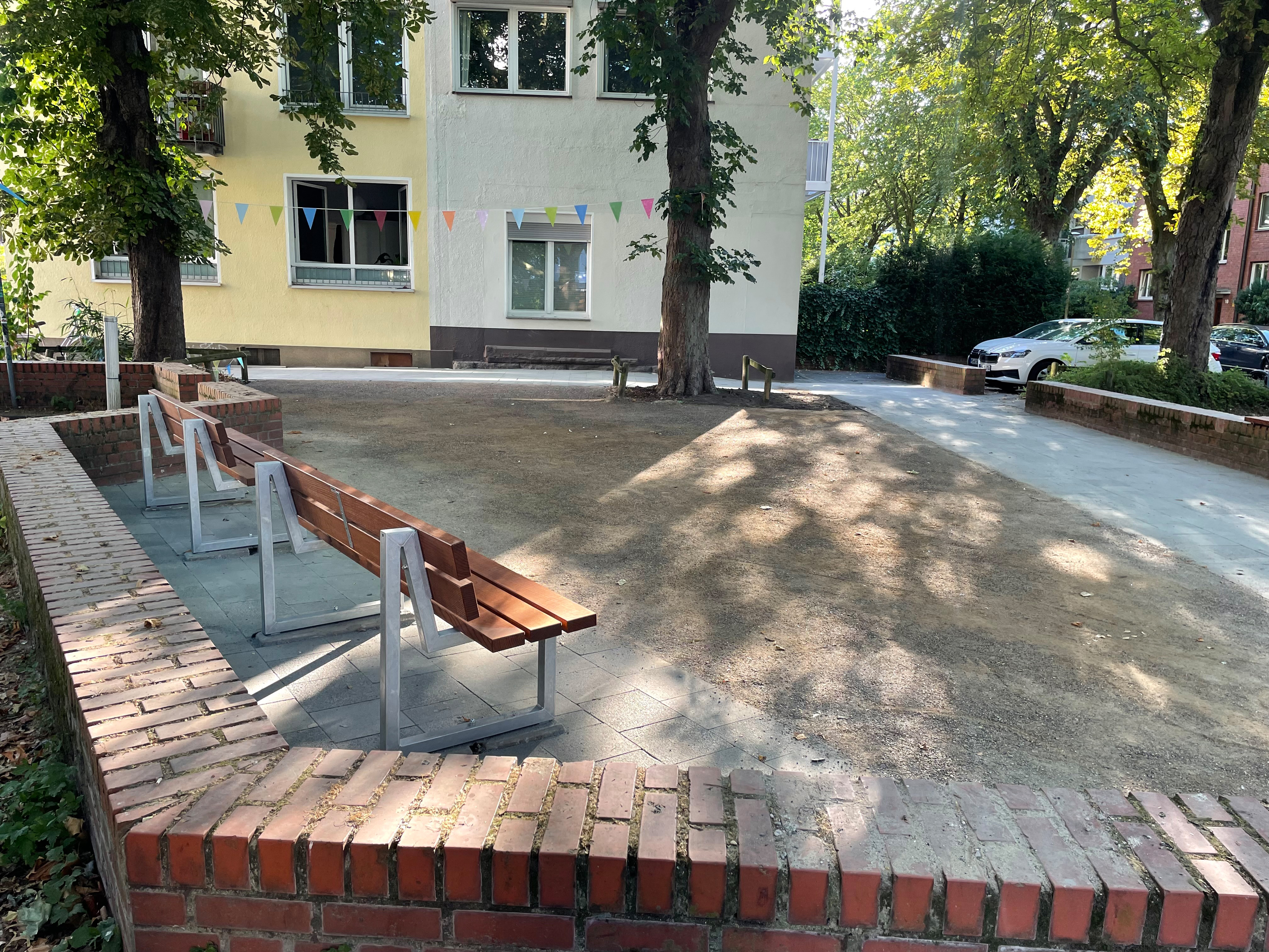 Drei neue Sitzbänke, davor eine Multifunktionale Fläche auf der etwa Boule gespielt werden kann. Der Platz ist dank Bäumen leicht beschattet.