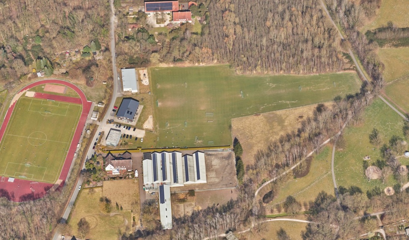 Blick auf die aktuelle Sportanlage am Wienburgpark, die Luftaufnahme zeigt das Sportfeld rechts, verschidene Gebäude in der Mitte und weitere Grünflächen im 