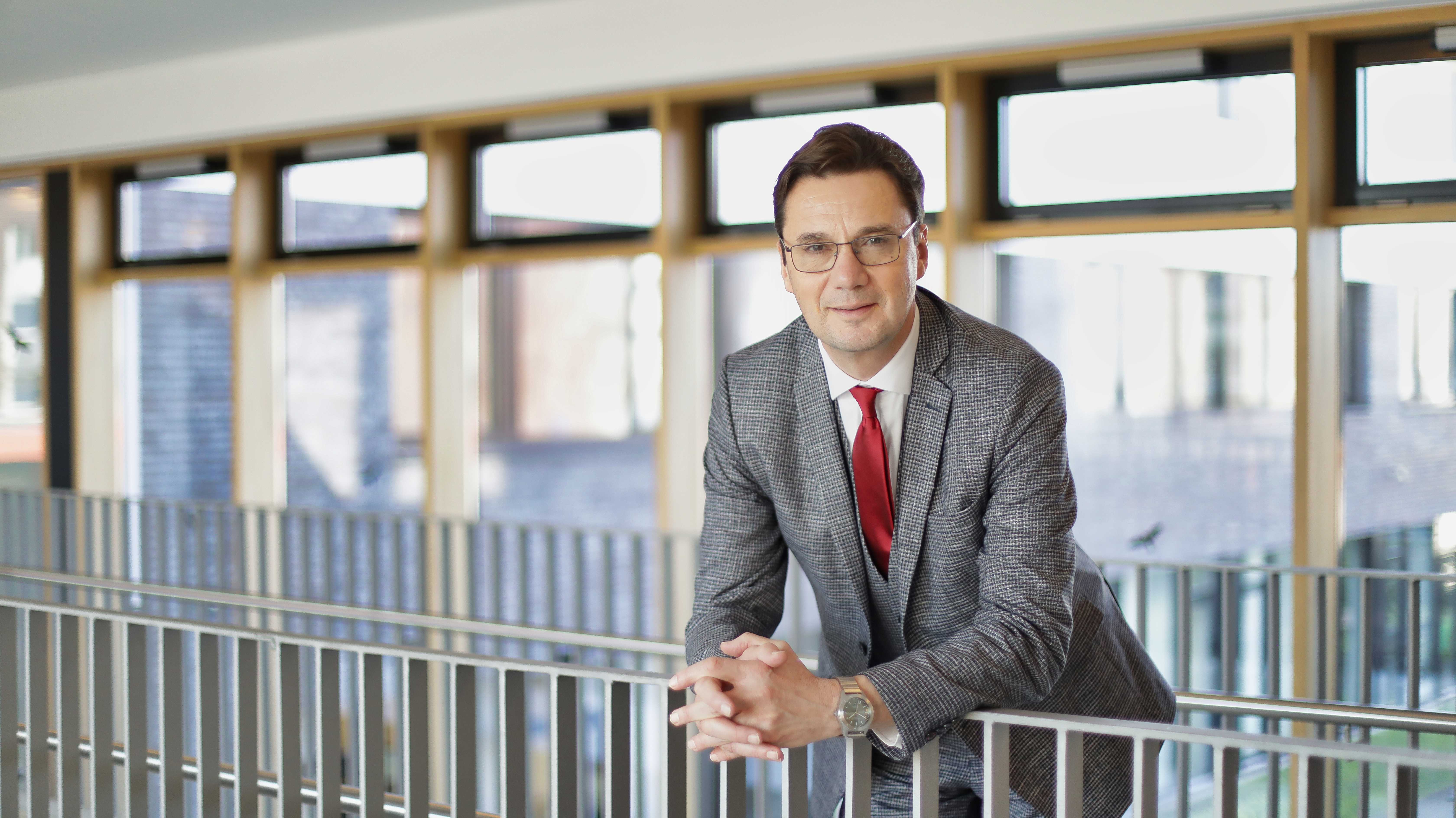 Stefan Wismann leht an einem Geländer, hinter ihm ist eine große Fensterfront