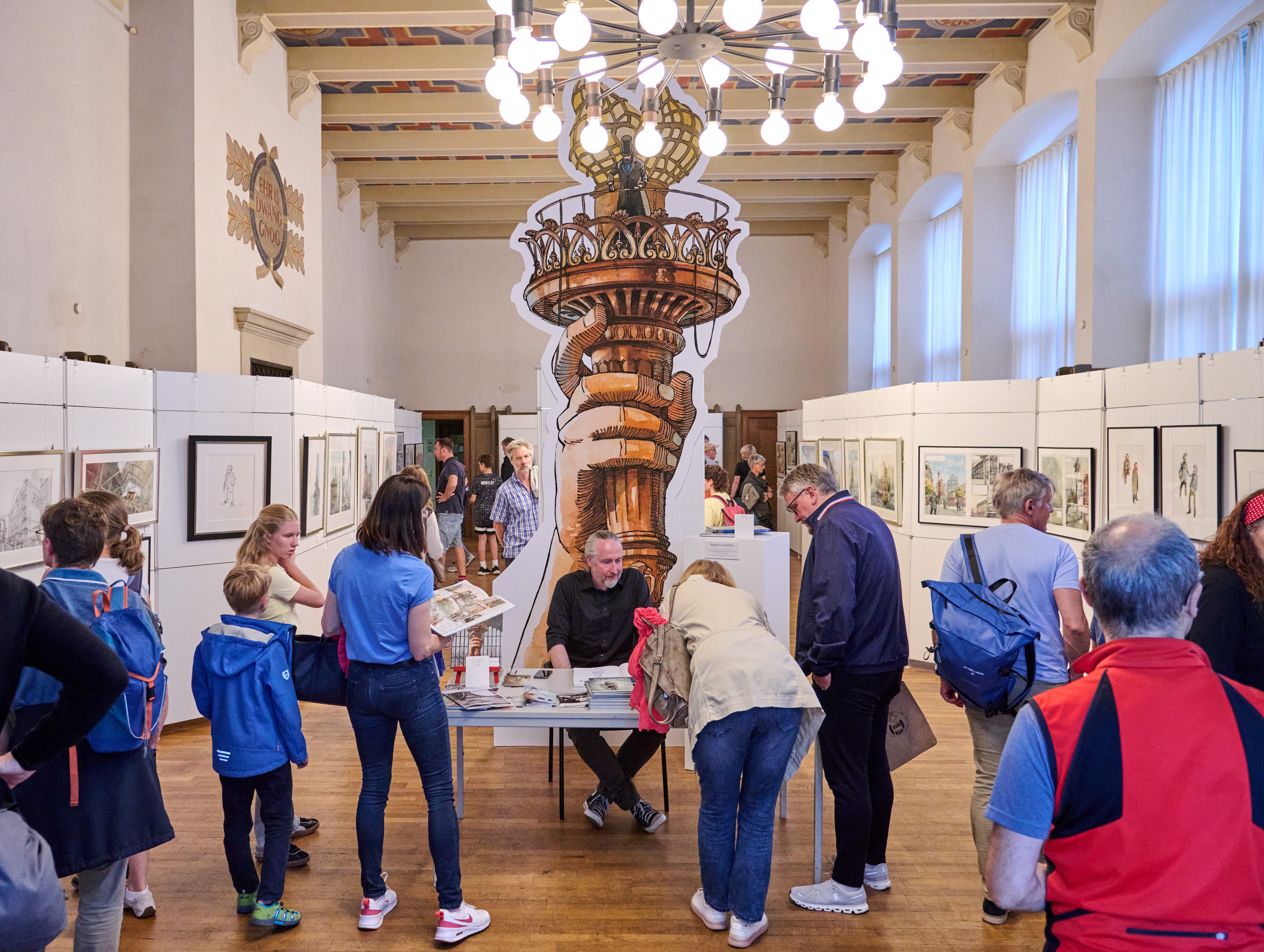 Interessierte Gäste schauen sich die Ausstellung im Krameramtshaus an, an einem Tisch sitzt der Künstler Jörg Hartmann und gibt Autogramme. 