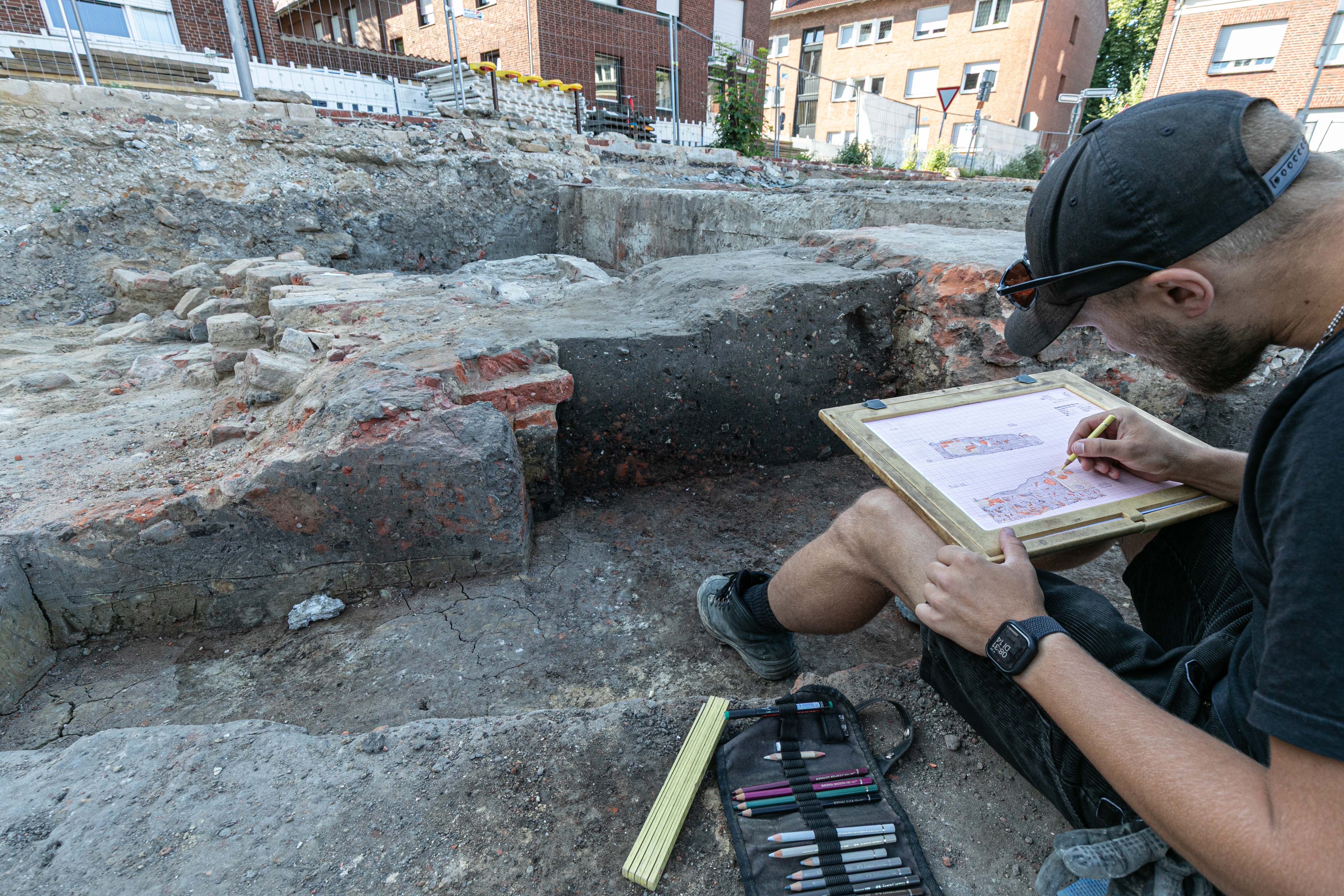 Ein Mitarbeiter der Stadtarchäologie Münster fertigt eine Zeichnung von Gebäudespuren an. Er sitzt in einem ausgegrabenen Bereich.