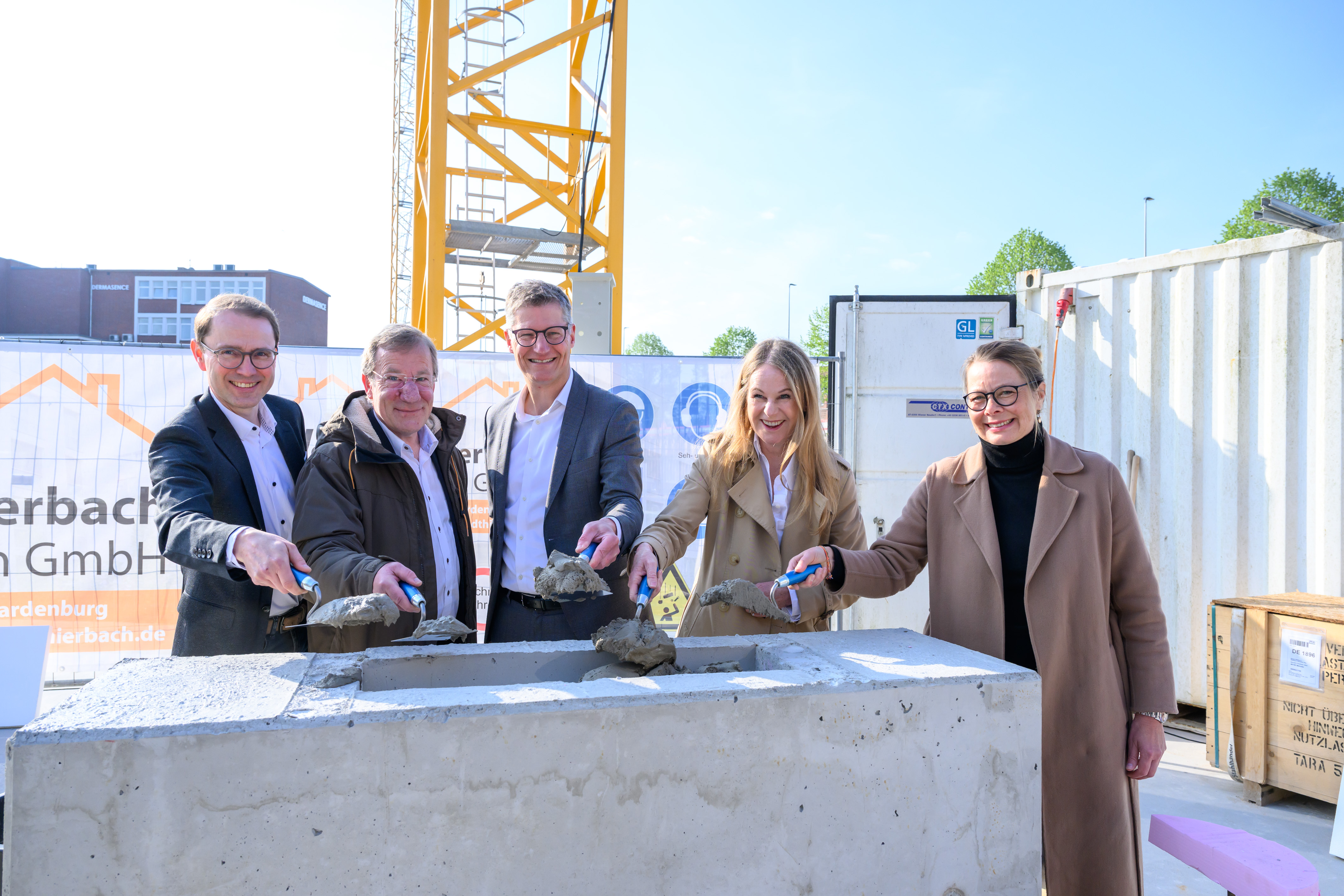 Gruppenfoto von fünf Personen, die mit einer kleinen Schaufel Sand in einen Stein schaufeln