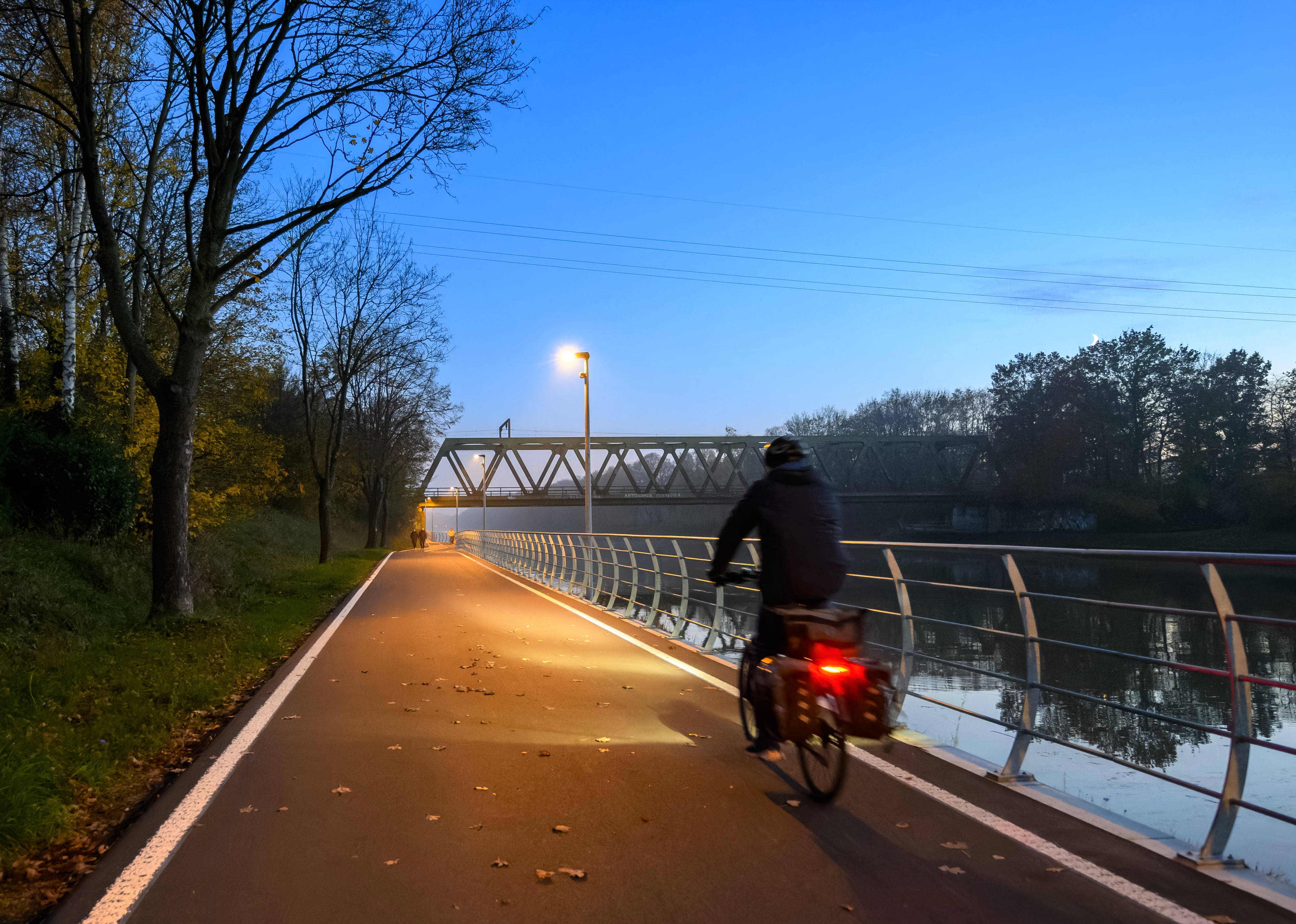 Eine radfahrende Person auf der Kanalpromenade bei Dämmerung
