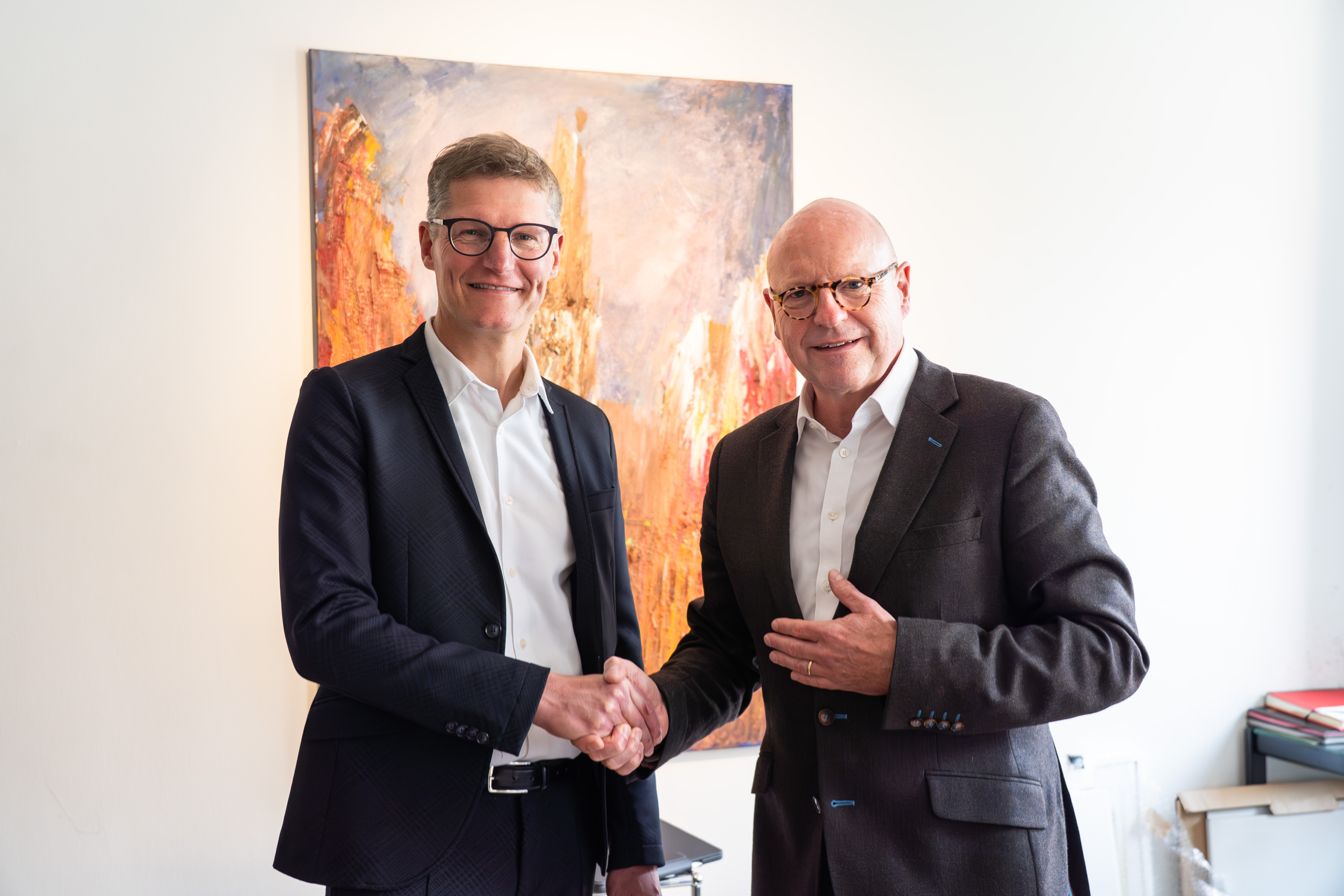 Zwei Männer schütteln sich die Hand und lächeln in die Kamera.