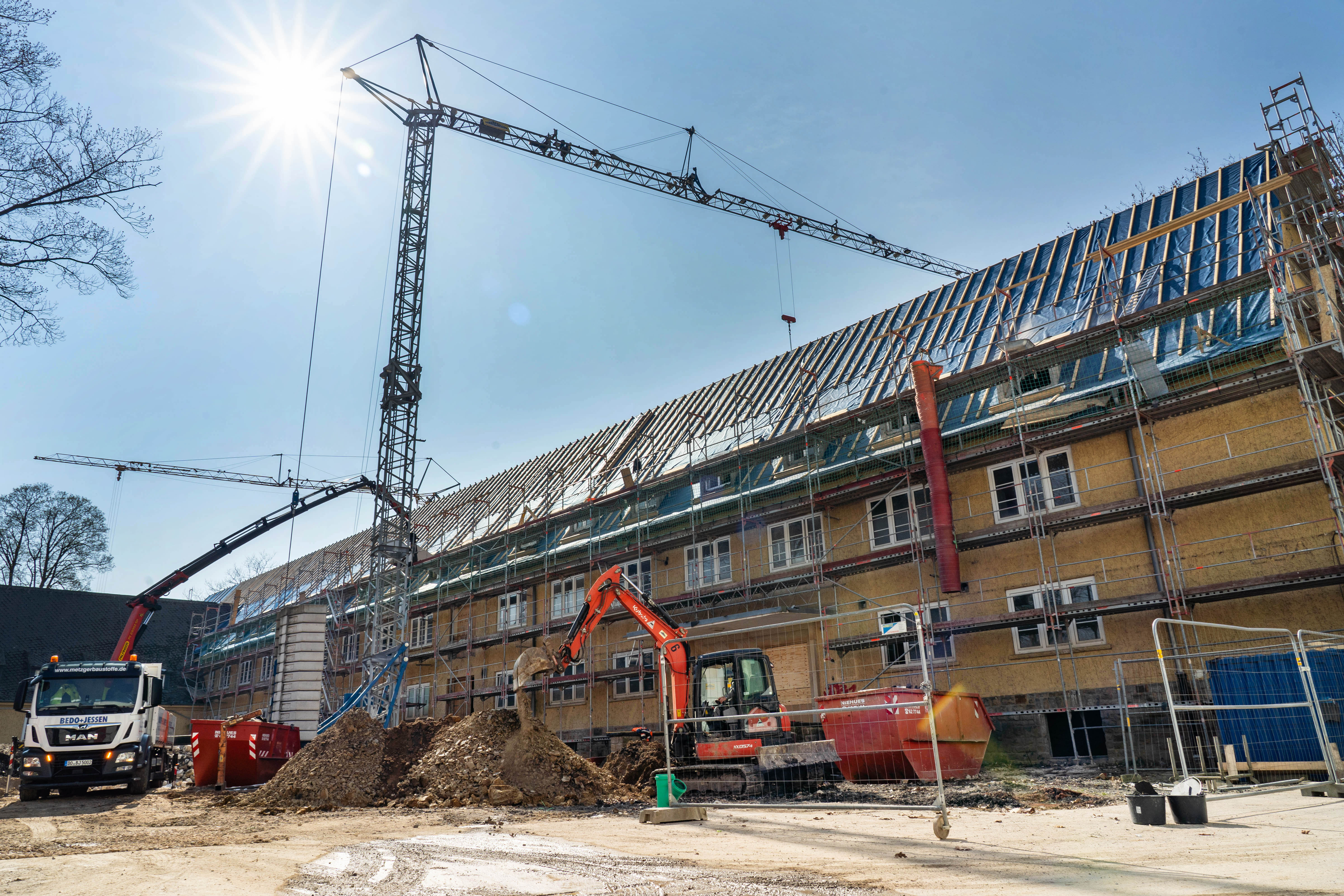 Blick auf die Baustelle des Gebäudes mit Baukran, Bagger, LKW und Baugerüst