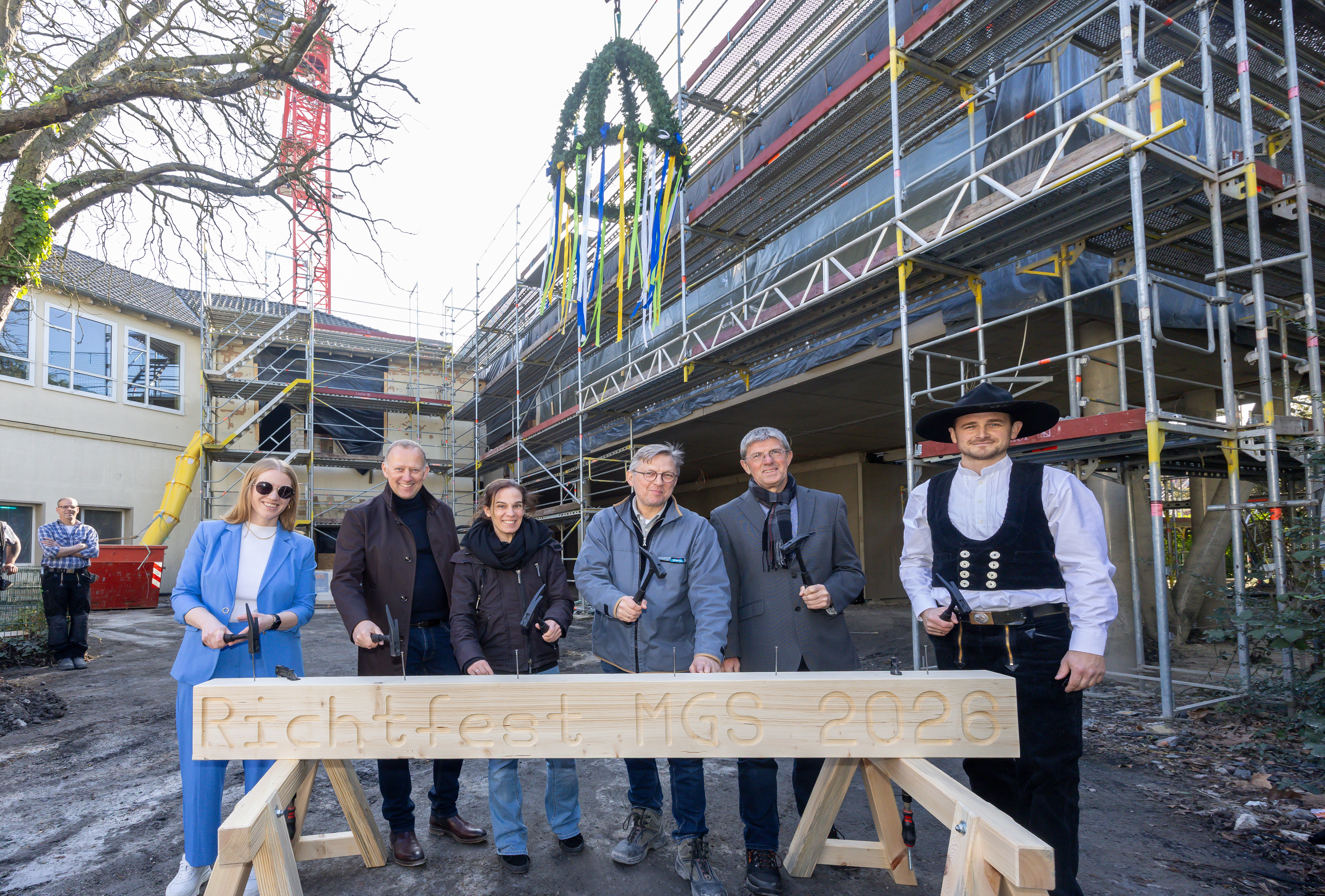Sechs Personen stehen hinter einem Holzbalken und hauen die letzten Nägel hinein