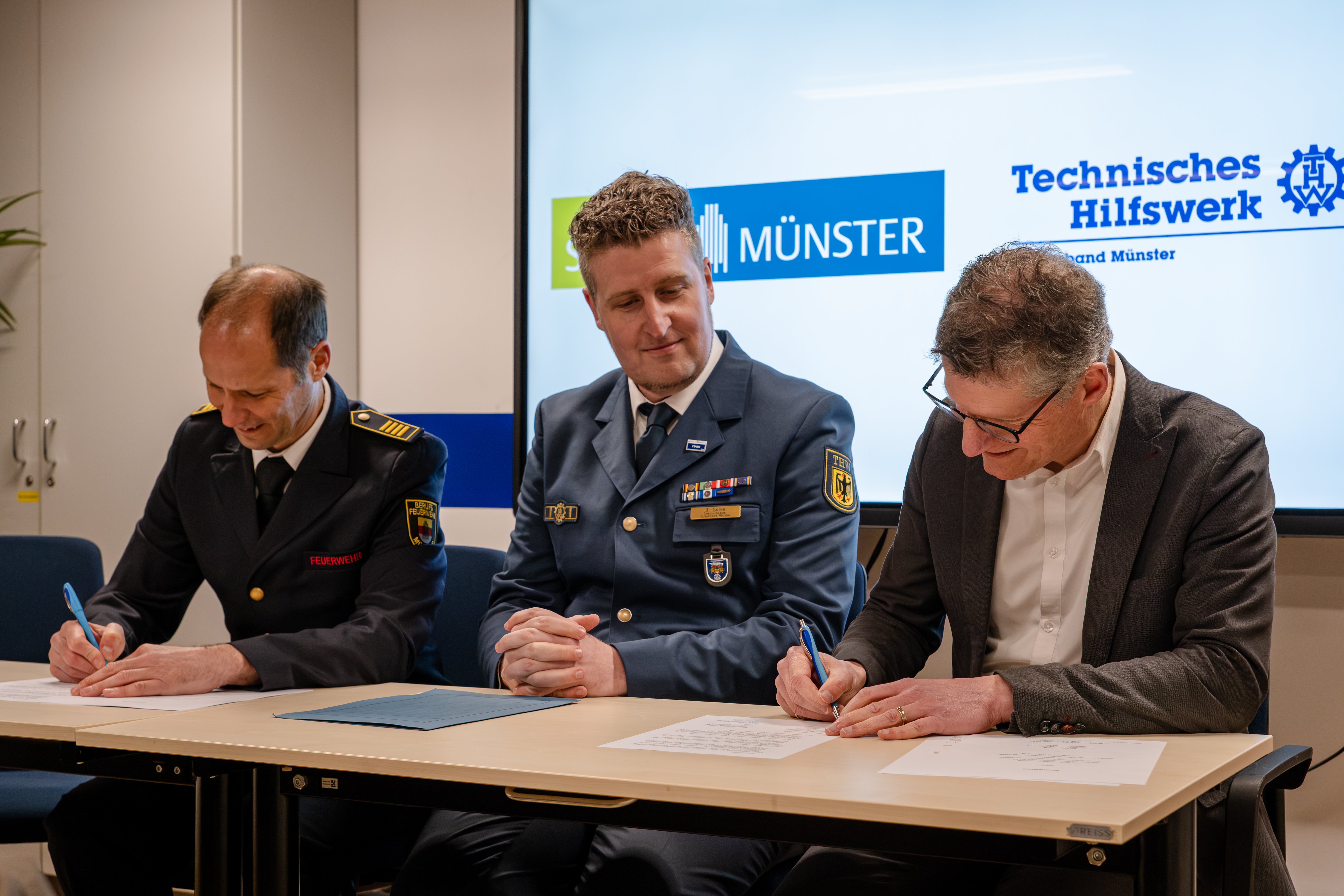 Oberbürgermeister Tilman Fuchs (r.), Gottfried Wingler-Scholz (l.), Leiter des Amtes für Bevölkerungsschutz, Feuerwehr und Rettungsdienst, bei der Unterzeichnung der Vereinbarung mit Bastian Solke, Ortsbeauftragter des THW-Ortsverbandes Münster.