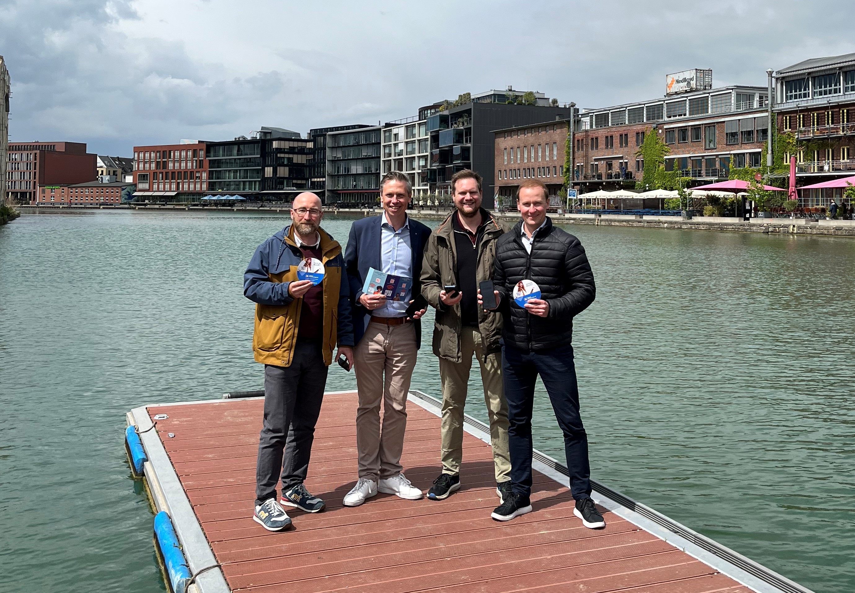 Vier Männer stehen auf einem Steg im Hafen.