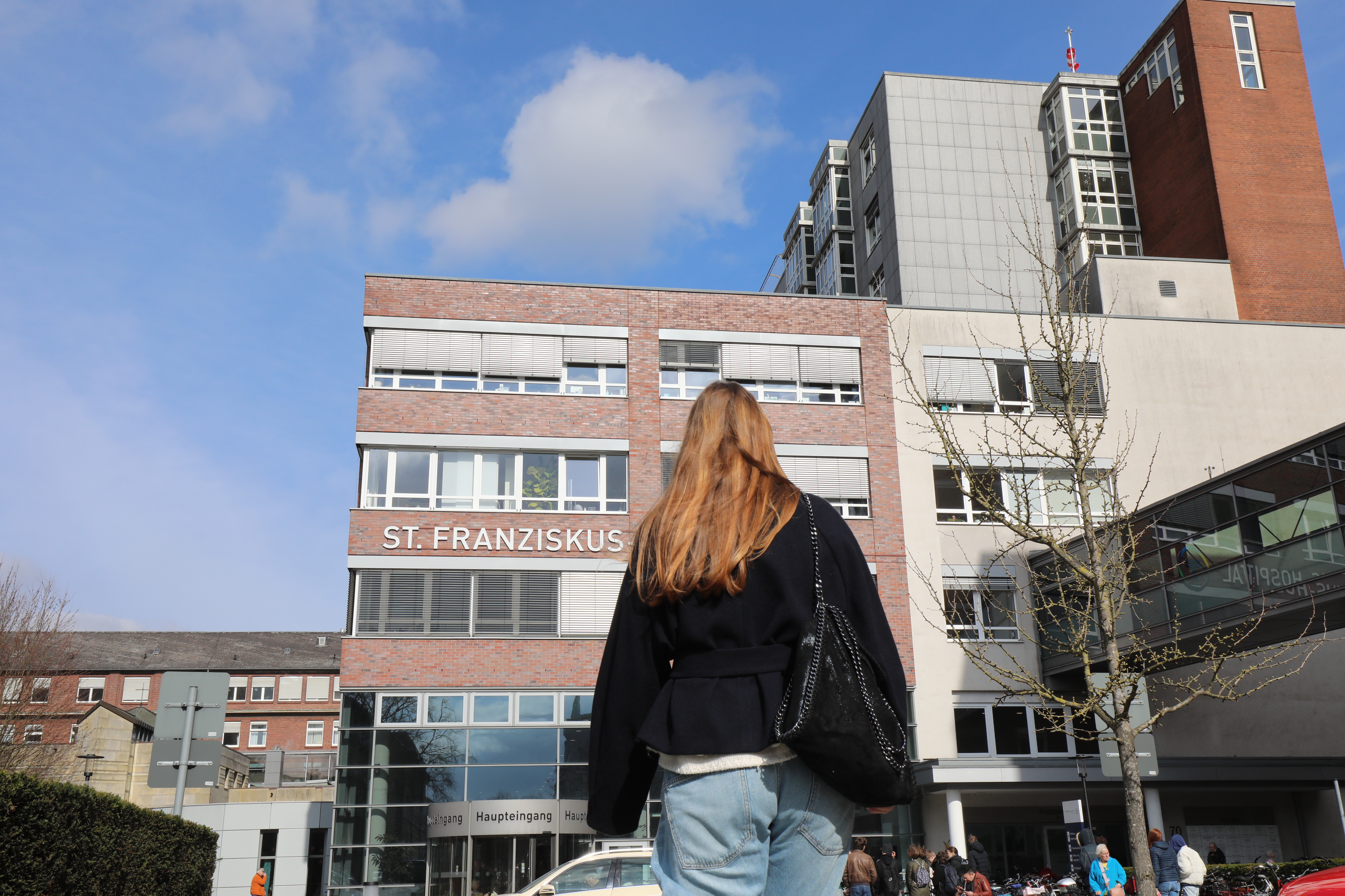 Eine junge Frau geht auf ein Krankenhaus zu.