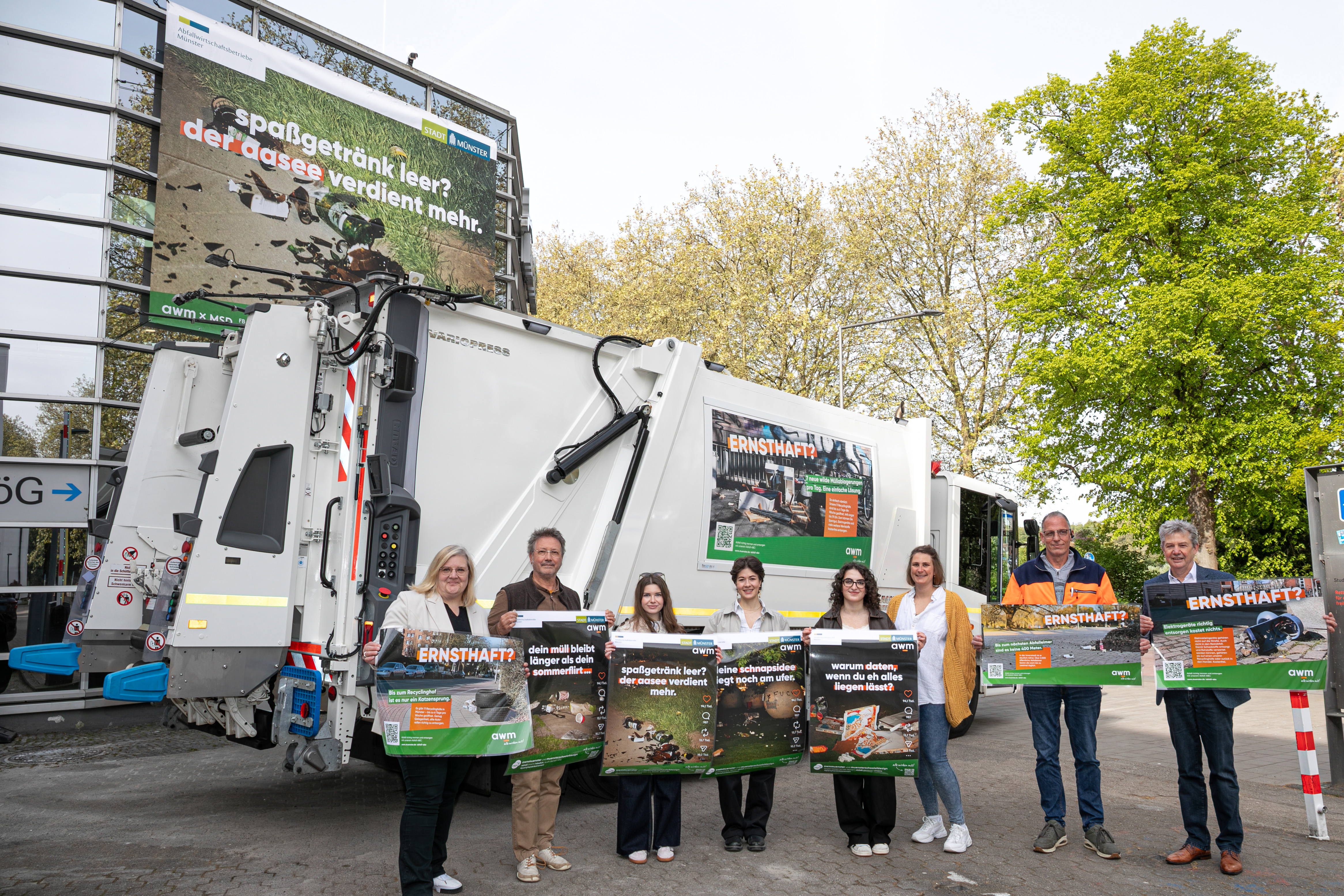 Acht Personen stehen vor einem Müllwagen und halten Plakate hoch.