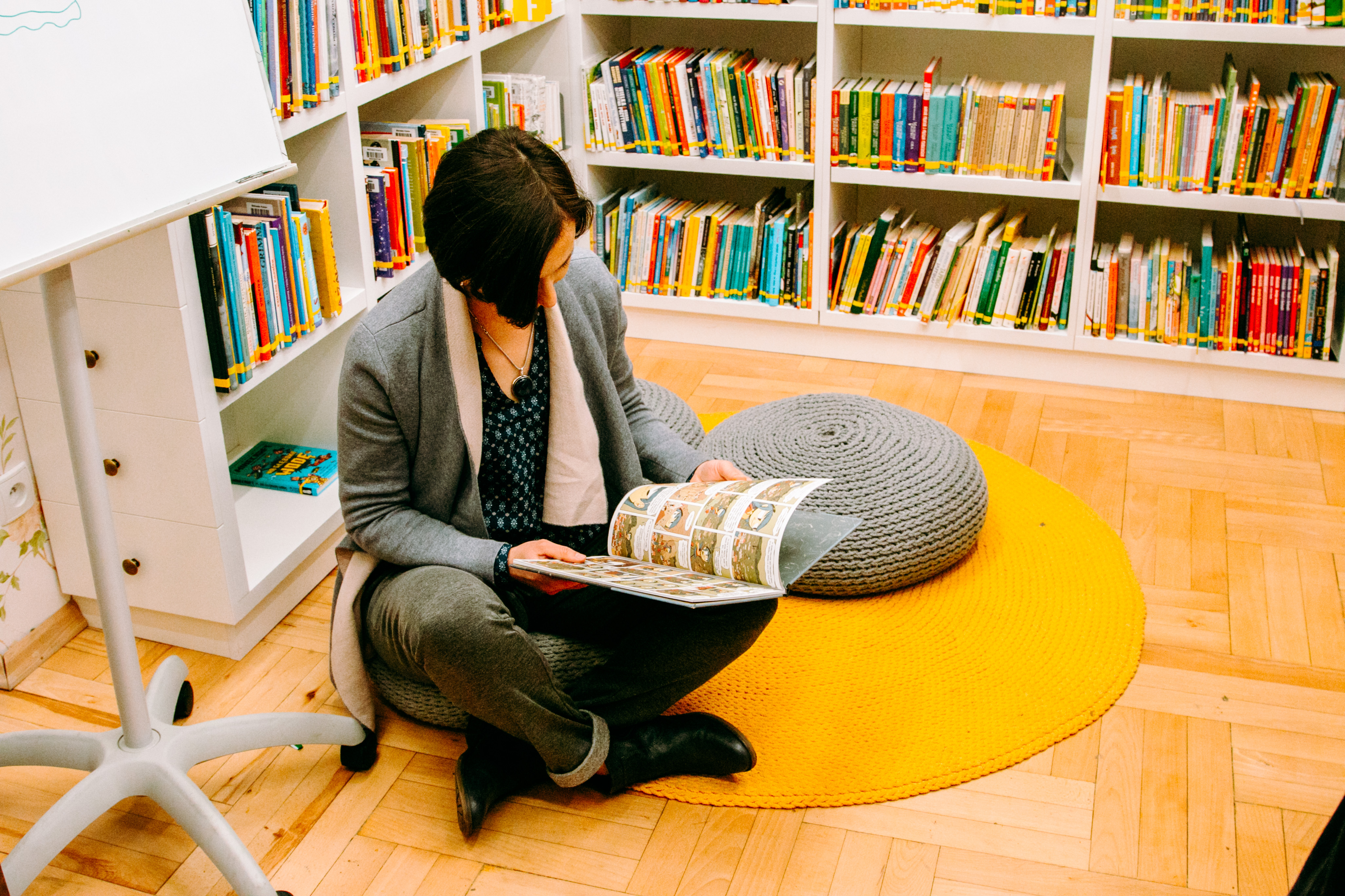 Frau im Schneidersitz auf dem Boden umgeben von Büchern liest ein Buch