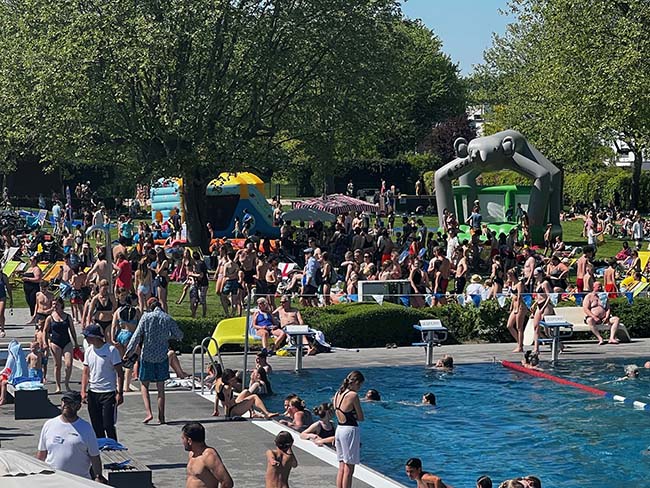 Besucher im vollen Freibad Coburg, im Vordergrund das Schwimmbecken und der Rand, im Hintergund die Wiese mit Bäumen