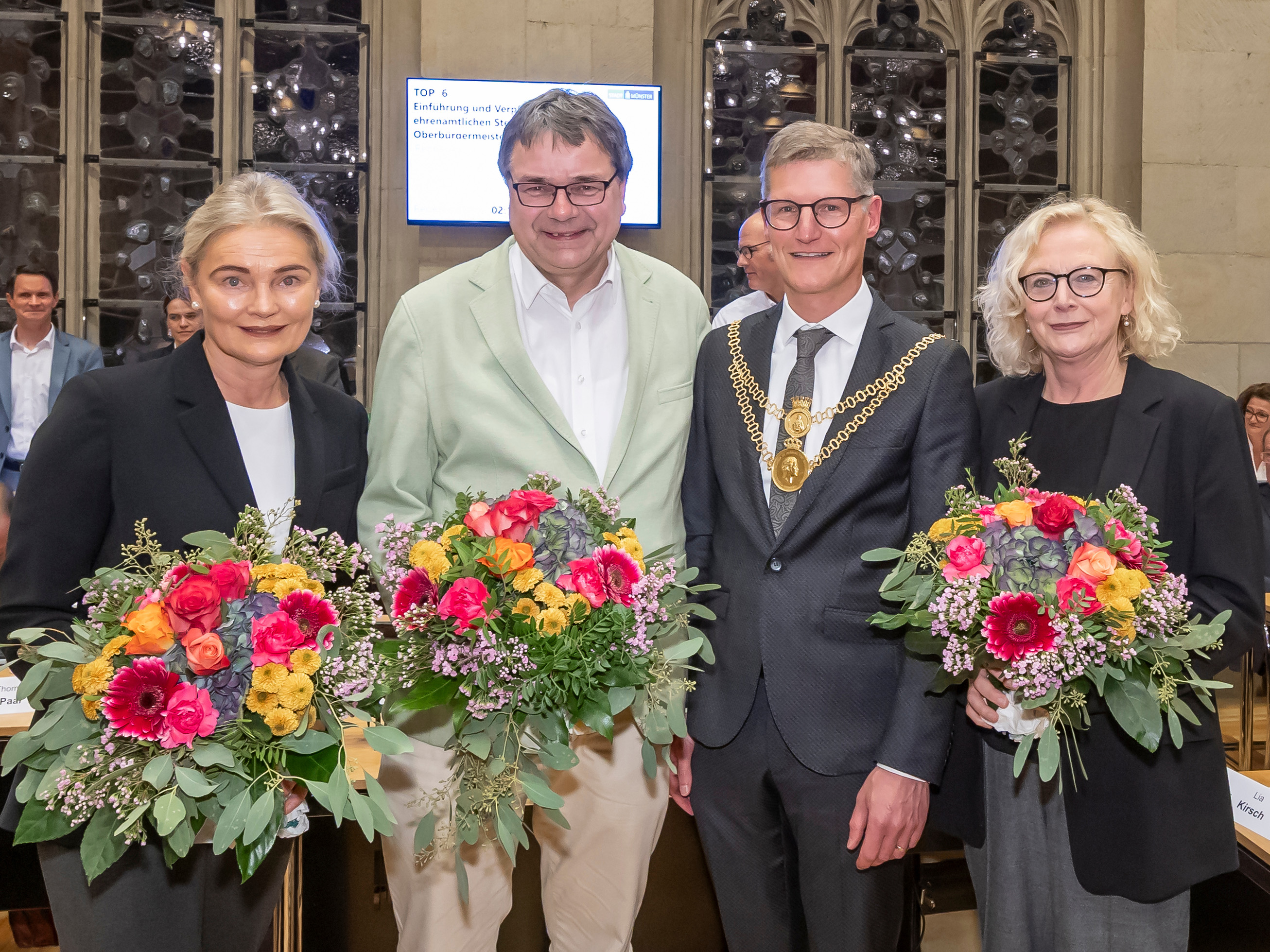Zwei Frauen und zwei Männer stehen in einer Reihe. Drei von ihnen haben einen Blumenstrauß in den Händen