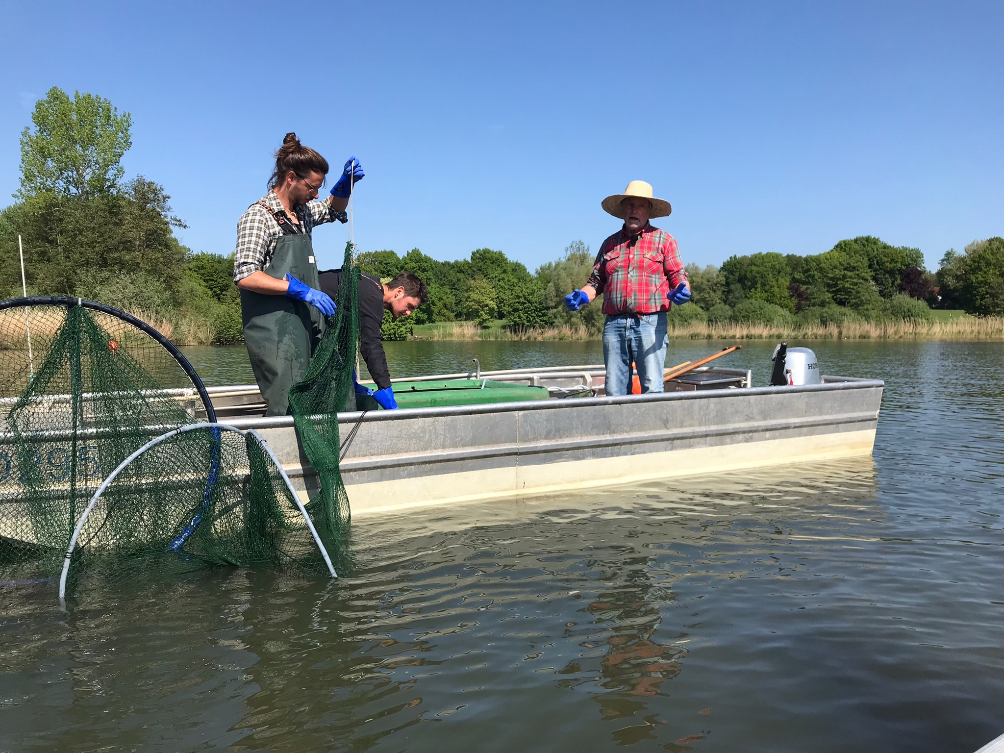 Drei Männer auf einem Boot mit Netzen zur Befischung auf dem Aasee
