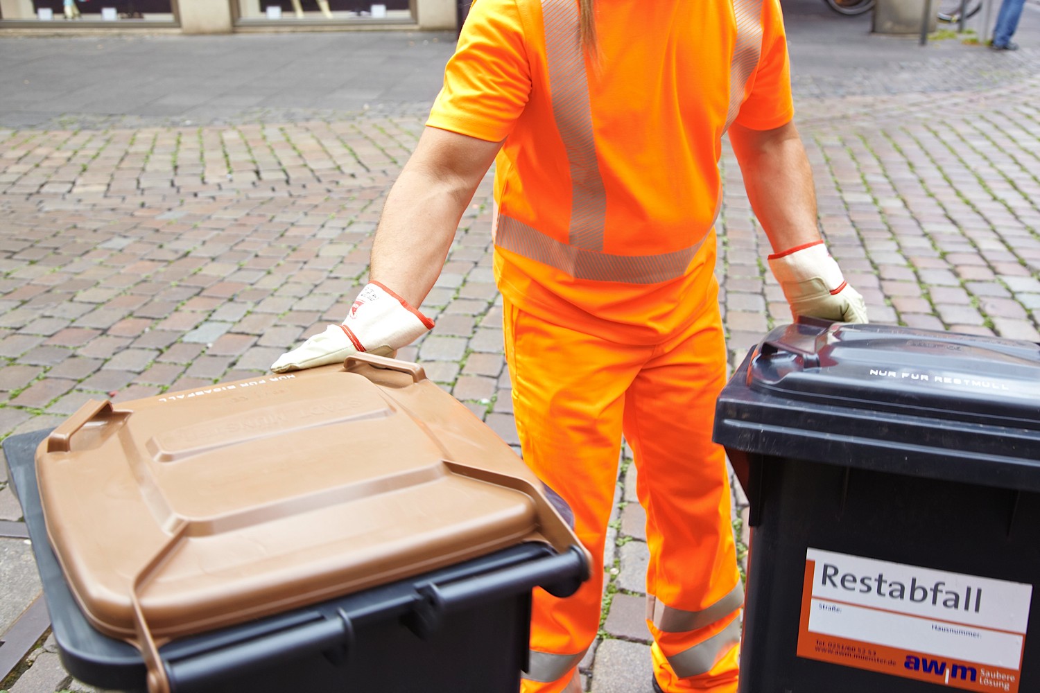 Zwei Abfalltonnen werden von einer Person gezogen