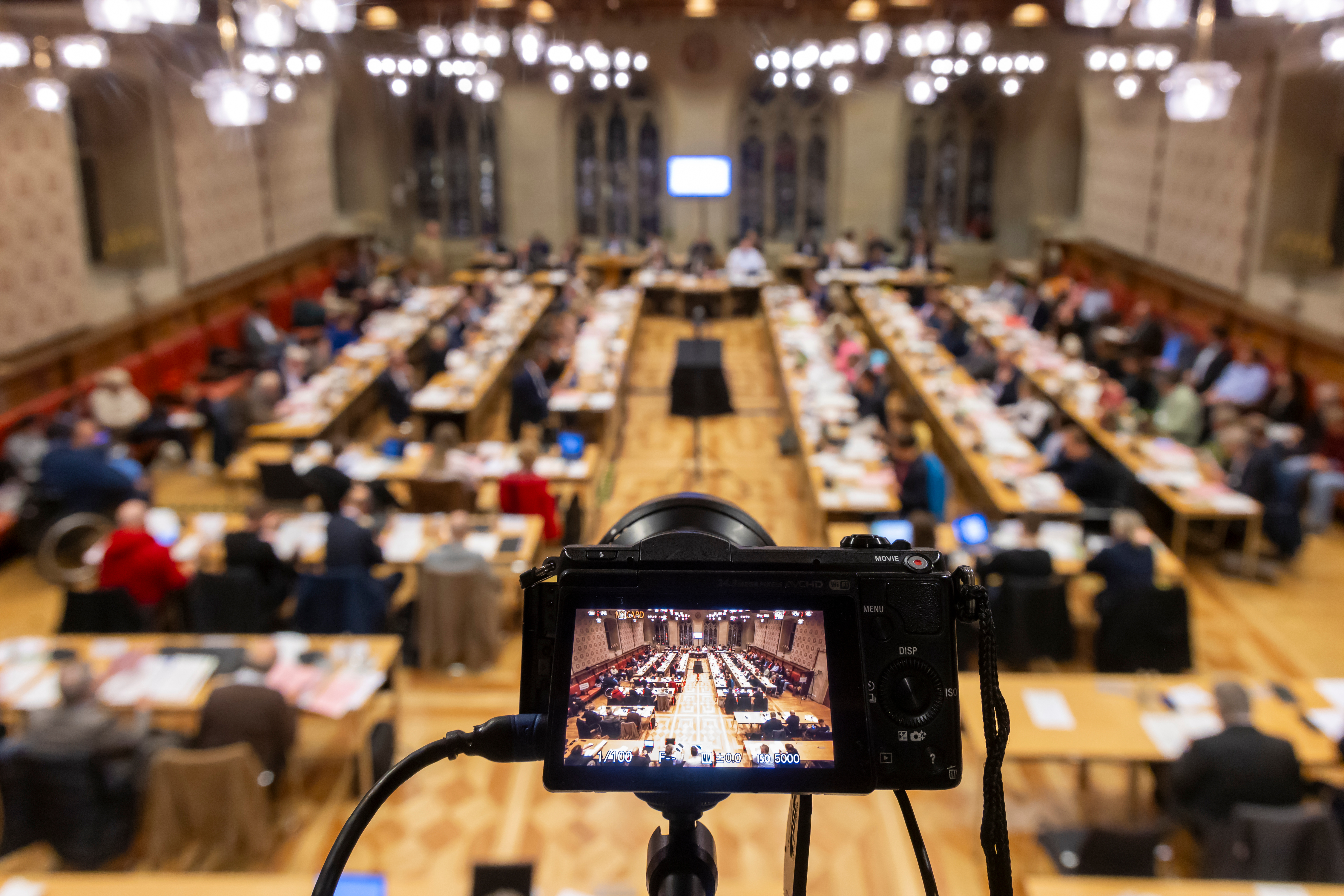 Blick auf die Ratssitzung im Rathausfestsaal, im Vordergrund eine Kamera, die ebenfalls auf die Sitzung gerichtet ist.
