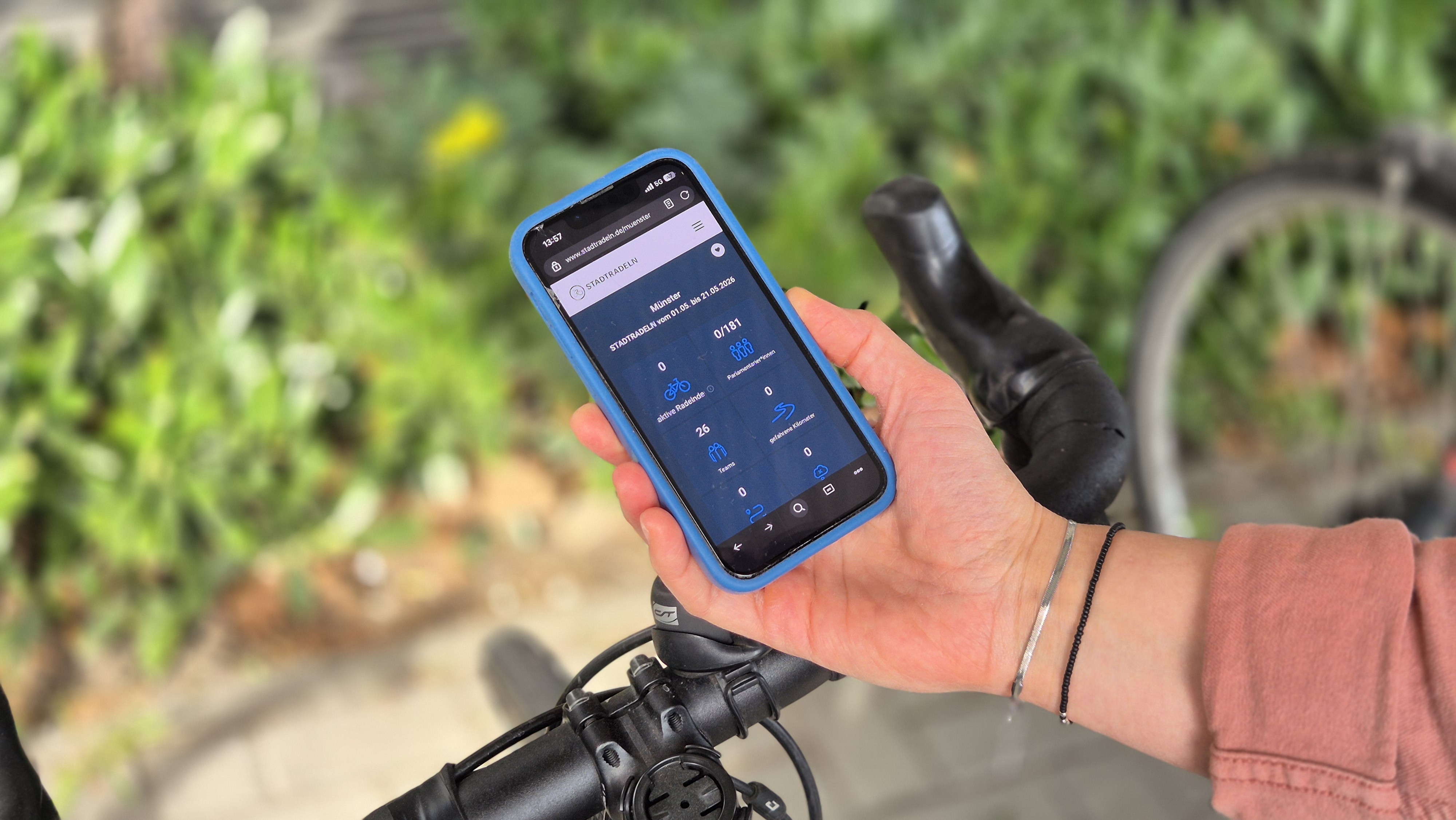Eine Hand hält ein Handy in der Hand, auf dem die Stadtradeln-App geöffnet ist. Im Hintergrund ein Fahrradlenker.