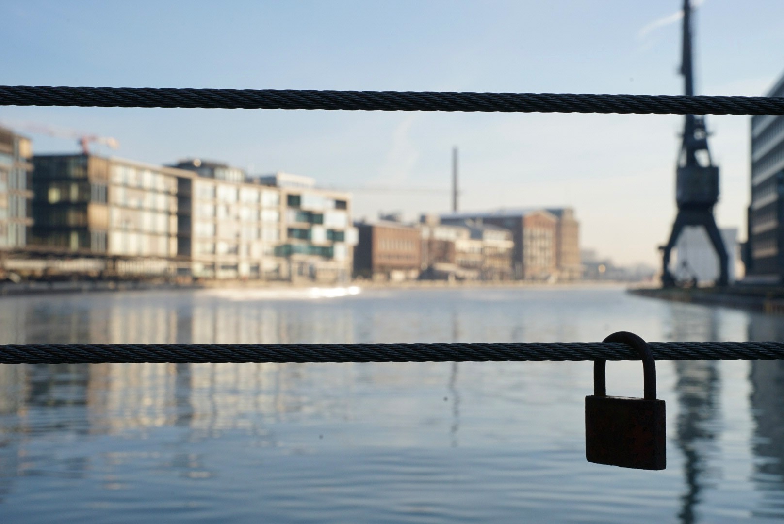 Ein Vorhängeschloss hängt an einem Geländer mit Blick auf den Hafen