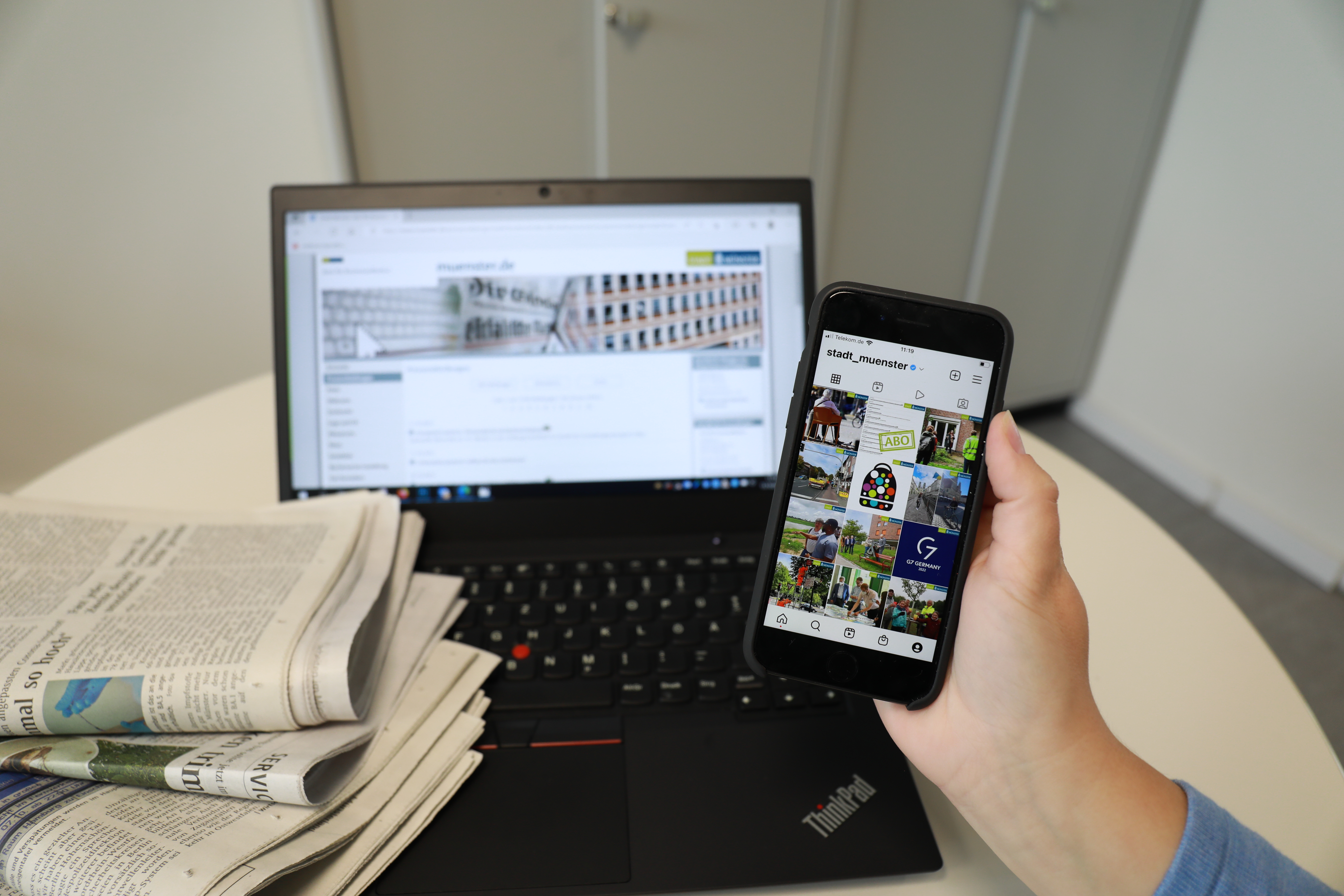 Laptop, Zeitungen und ein Smartphone in der Hand