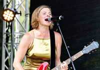 Die Musikerin Bernadette La Hengst im goldenen Kleid mit roter Elektrogitarre auf der Bühne