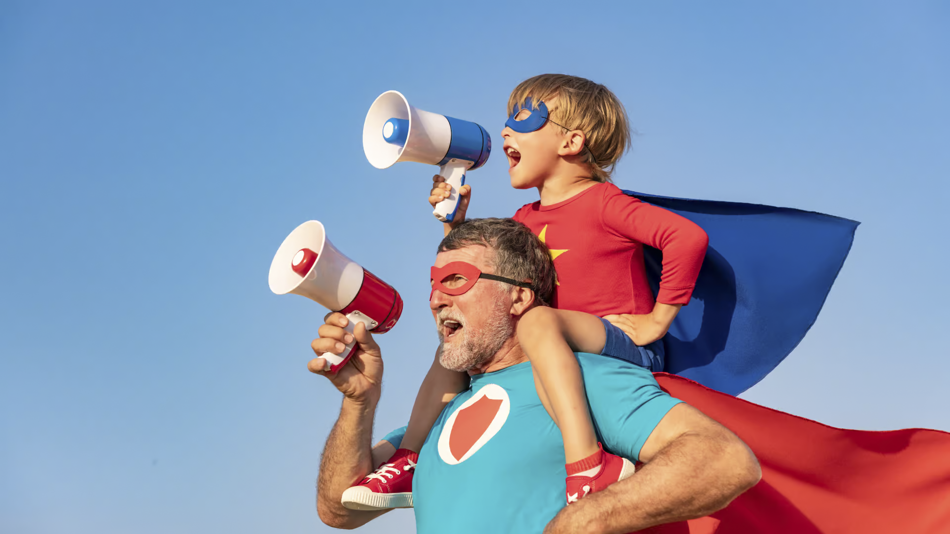 Vater und Sohn als Superhelden verkleidet rufen jeweils in ein Megafon