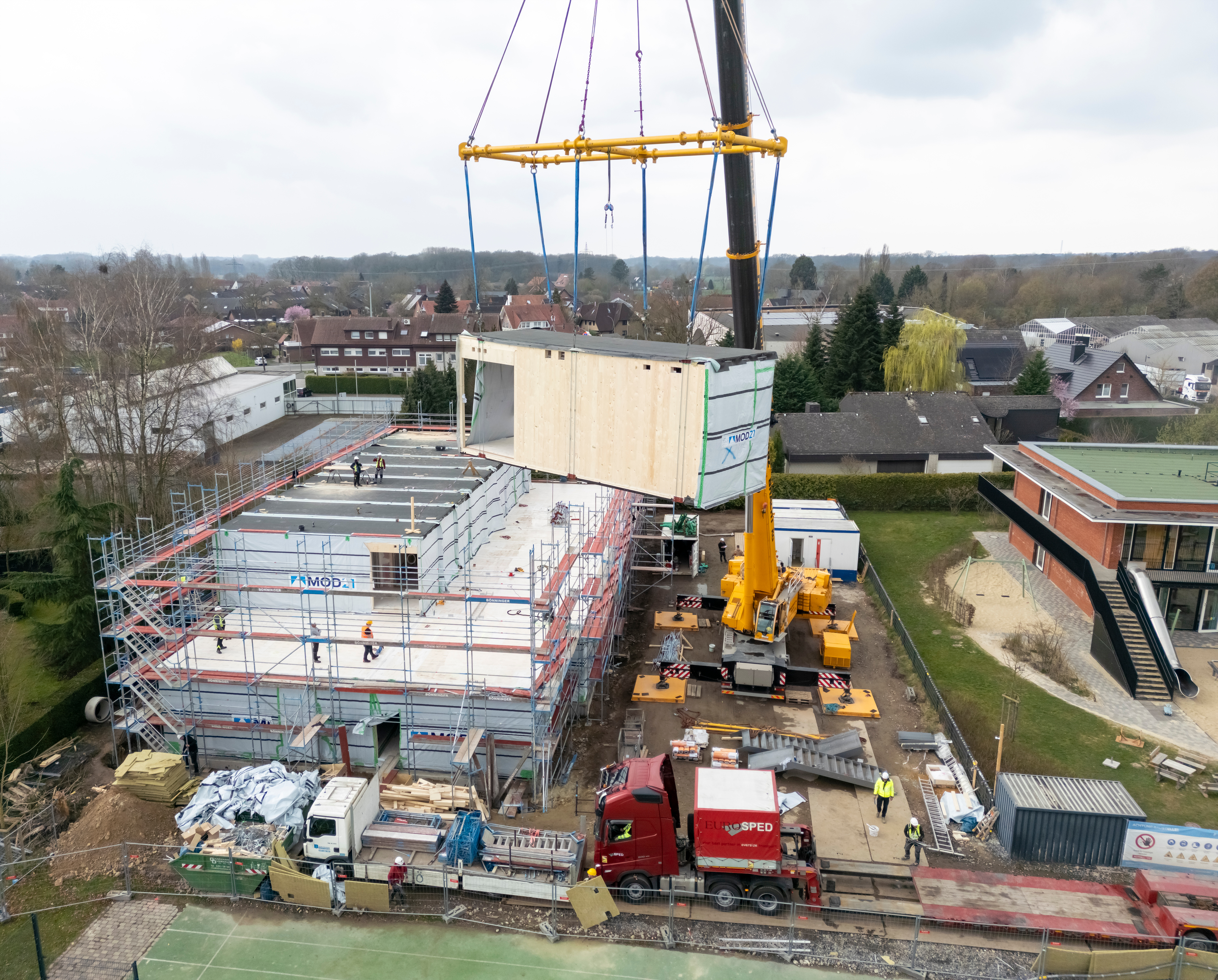 Eines der Module schwebt hängend am Baustellenkran über der Baustelle