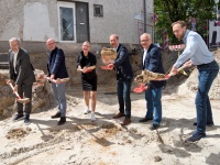 Foto: Fünf Männer und eine Frau werfen mit einem Spaten Sand in die Luft.