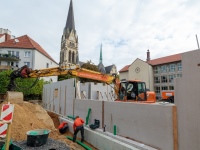 Ein Bagger schaufelt Sande über die neuen Wände, im Hintergrund ist die Kreuzkirche zu sehen.