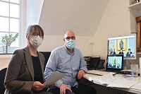 Eine Frau und ein Mann mit Mund-Nasen-Bedeckung vor einem Computer