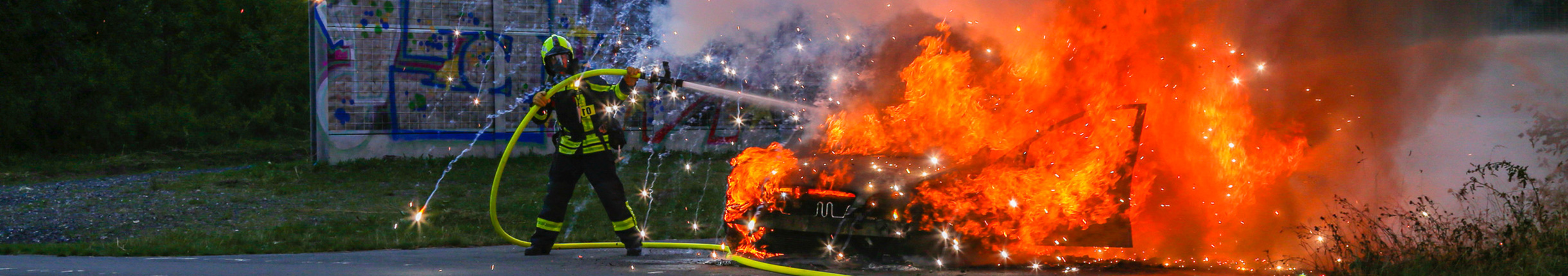 Ein Feuerwehrmann löscht zur Übung ein brennendes Fahrzeug