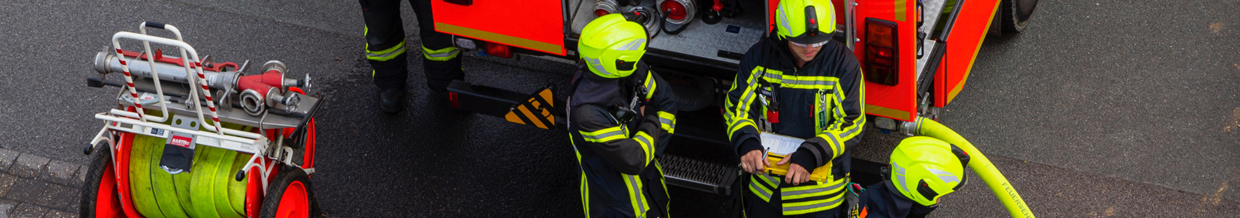 Luftaufnahme: Drei Feuerwehrleute an der Rückseite eines Feuerwehrfahrzeugs.