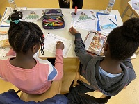 Zwei Kinder sitzen an einem Tisch mit Büchern und Zetteln