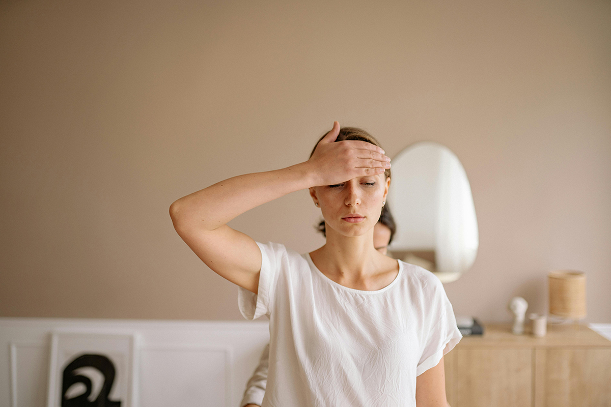 Junge Frau praktiziert zuhause eine Entspannungsübung, indem sie ihre Hand auf die Stirn legt.