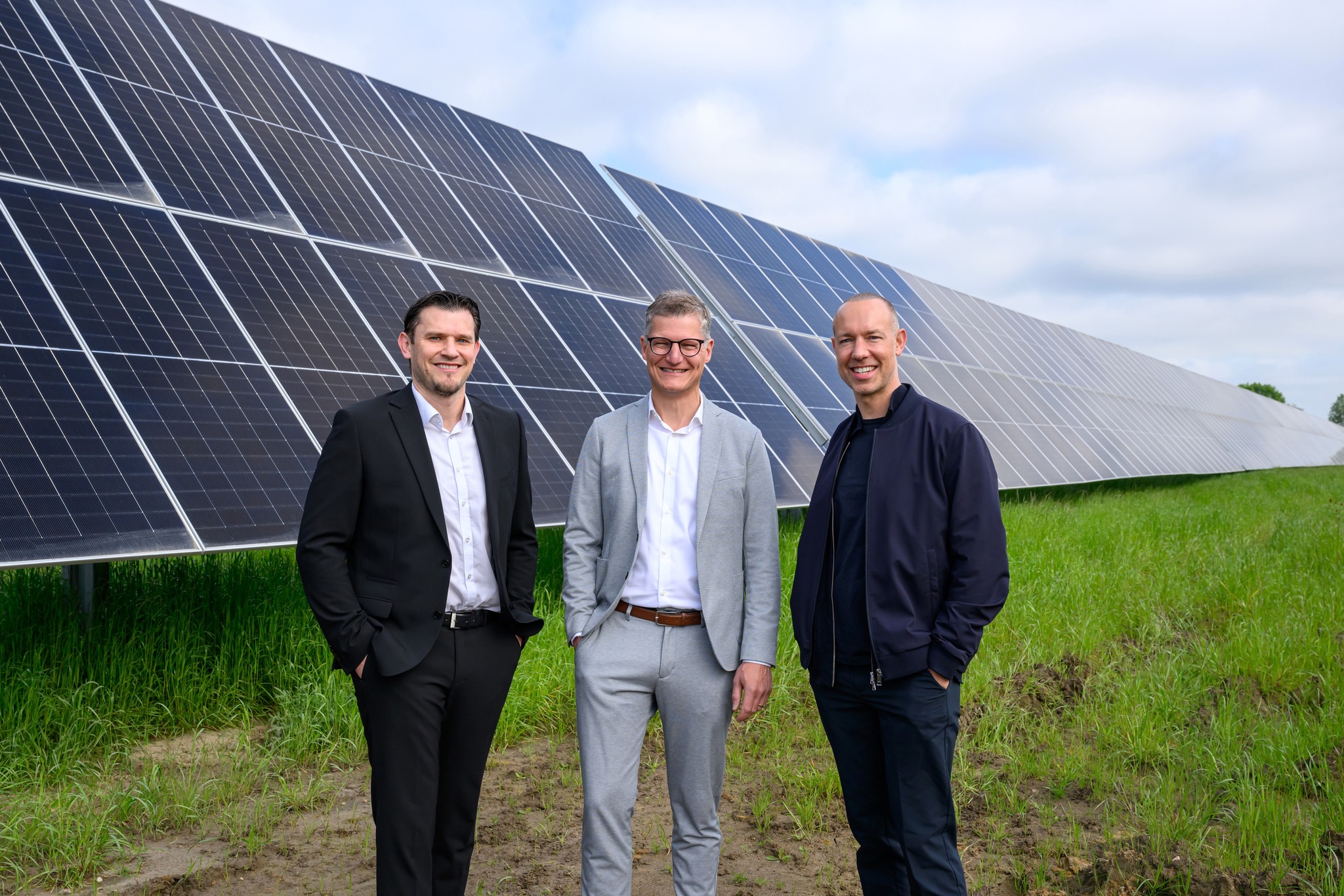 Drei Männer in Anzügen vor hochaufstellten Solar-Modulen auf der Wiese
