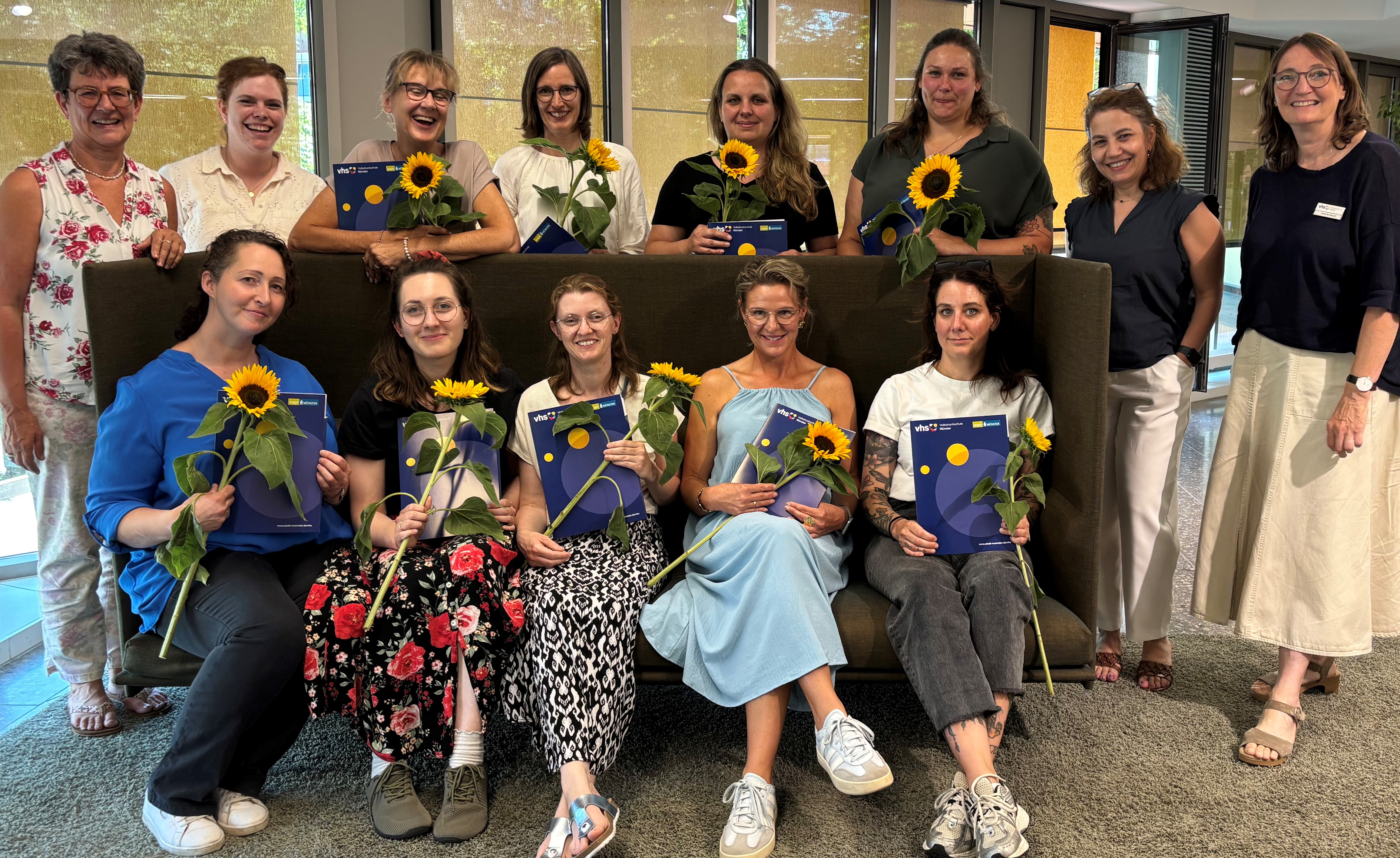 Gruppe teils sitzend auf Sofa, teils stehend, mit Sonnenblume und Zertifikat