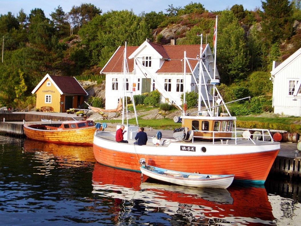 Ein rotes Segelboot liegt in Kristiansand am Kai mit Wohnhäusern und viel Grün im Hintergrund.