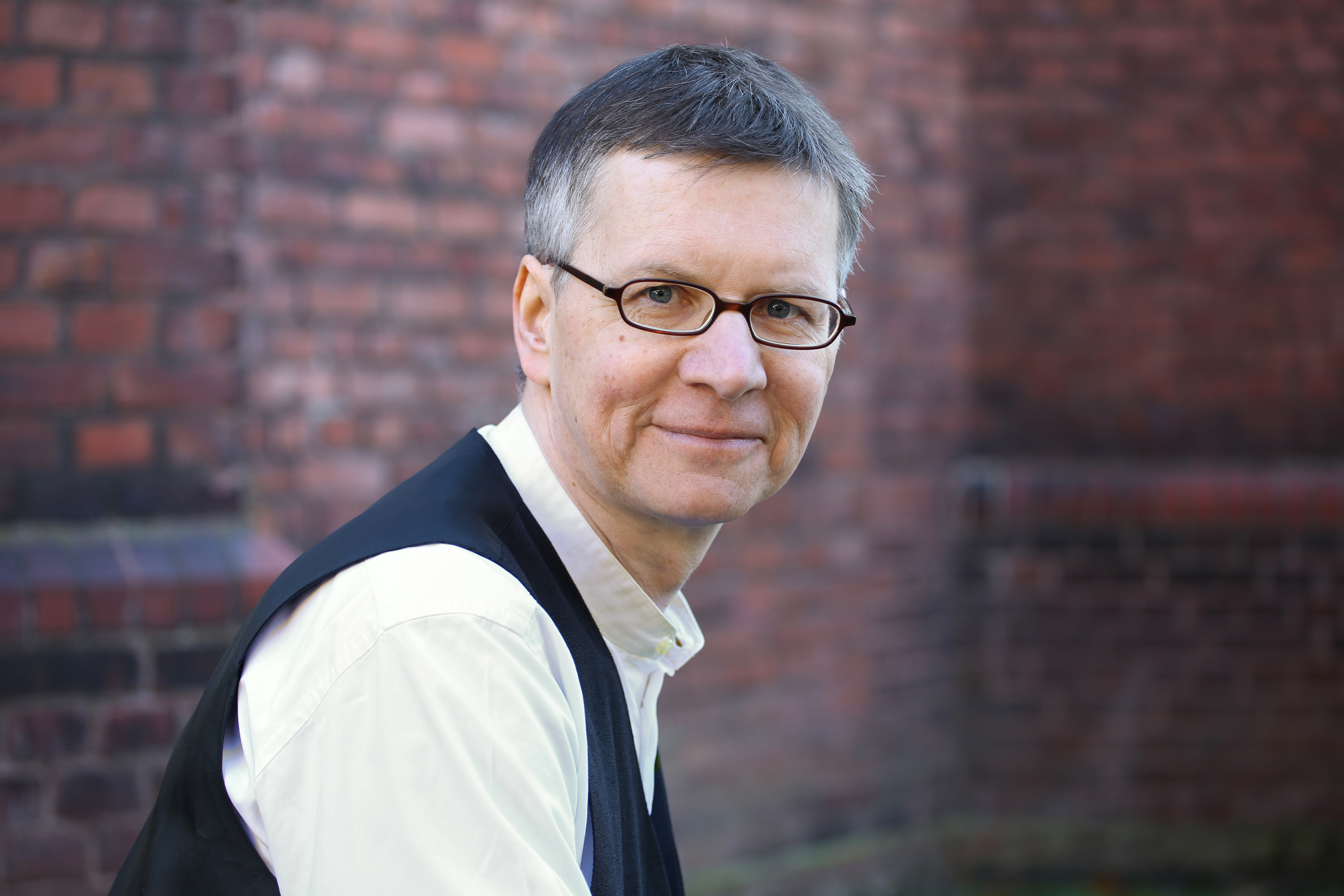 Kurzhaariger Mann mit Brille und weißem Hemd mit dunkler Weste