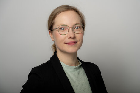 Frau mit Brille und mit Zopf, bekleidet mit blauem Jacket