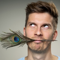Portraitaufnahme von Simon Stäblein mit Pfauenfeder im Mund