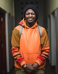 Foto des Autors Kagayi Ngobi in einem orangenen Pullover.
