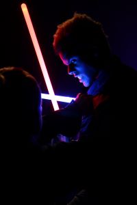 Zwei Menschen bekämpfen sich im Dunkeln mit Laserschwertern. Lediglich das Gesicht des einen Mannes ist im Schein der Schwerter zu erahnen.